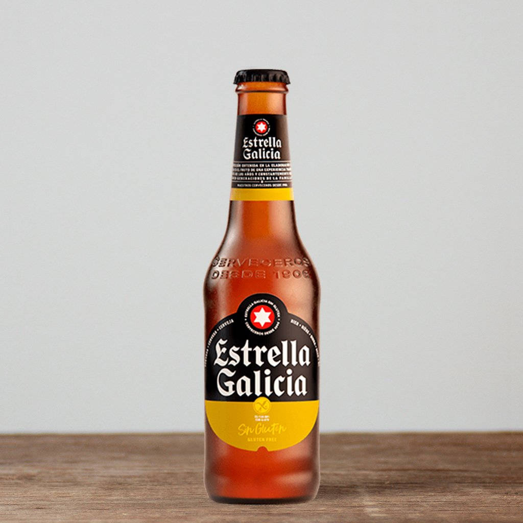 alcohol 桌布 壁紙 — 一支琥珀色的Estrella Galicia啤酒瓶，帶有無麩質標籤，直立於木質表面上，背景為中性灰色。