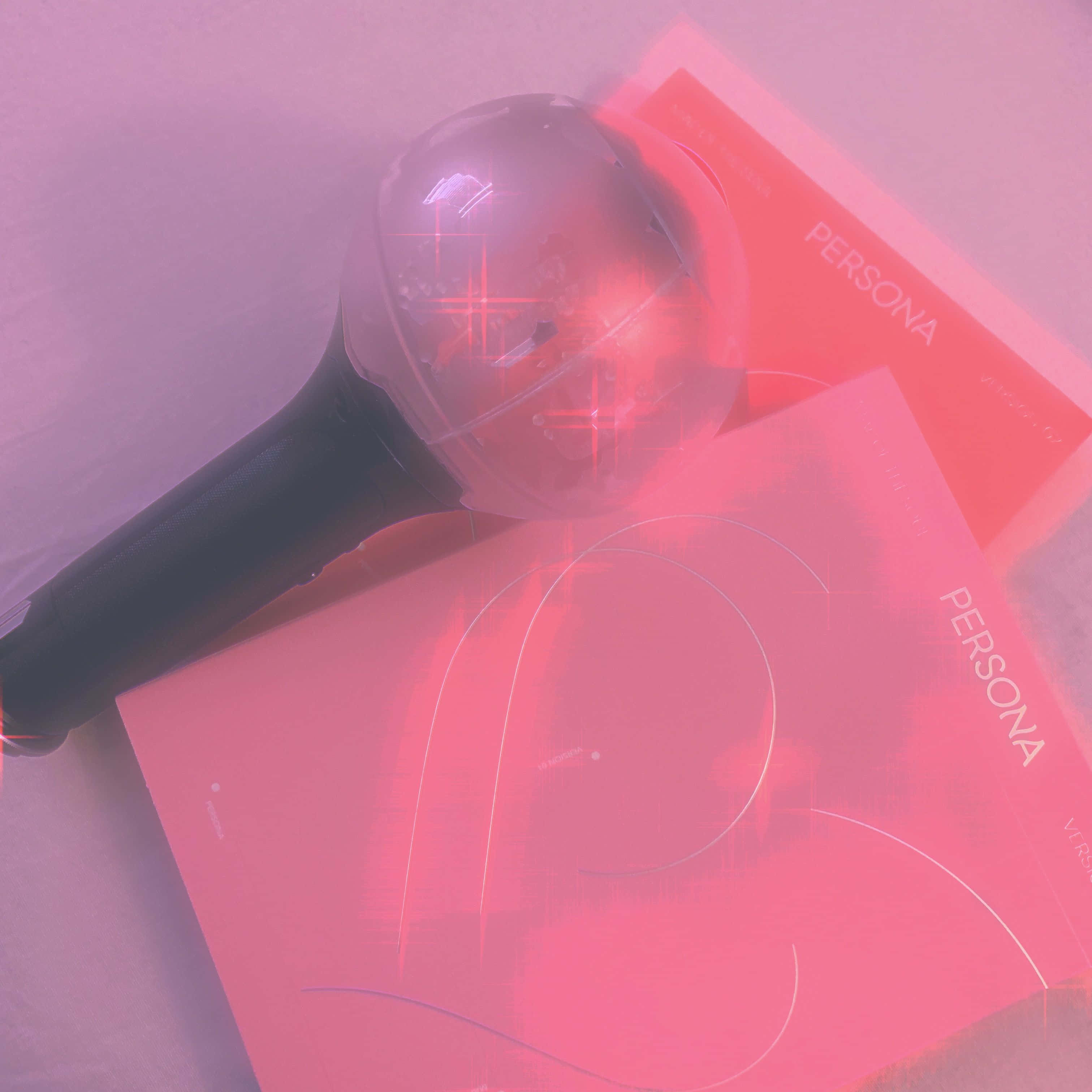 Bts Army Bomb 桌布 壁紙 — 一支發光的粉紅色應援棒放在兩張「PERSONA」專輯封面上，在柔和粉紅和紫色燈光下。