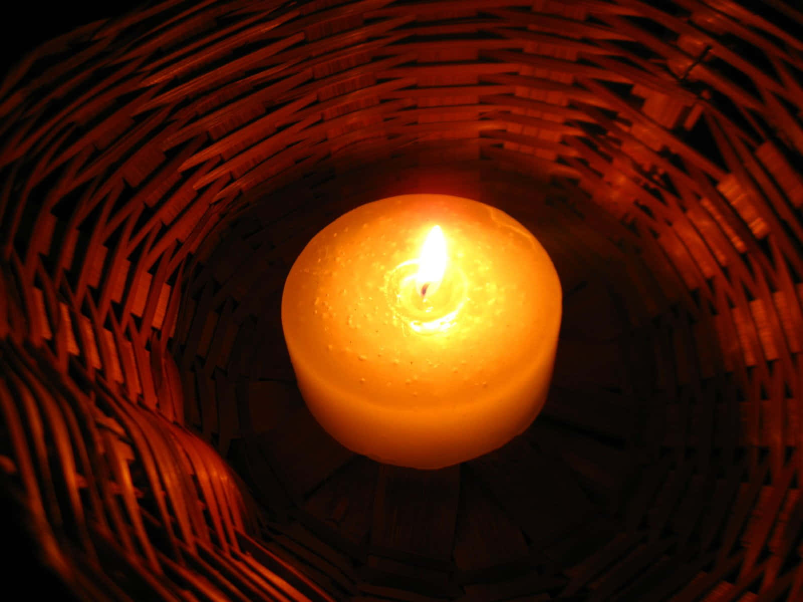 Candle Light 桌布 壁紙 — 一支發光的蠟燭安放在深色編織籃中，在舒適私密的環境中散發出溫暖的琥珀色光芒。