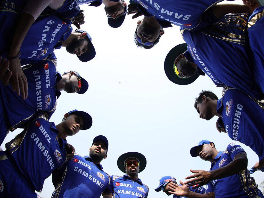 Mumbai Indians 桌布 壁紙 — 一支穿著藍色三星球衣的板球隊在明亮的日光下緊密圍成一圈。