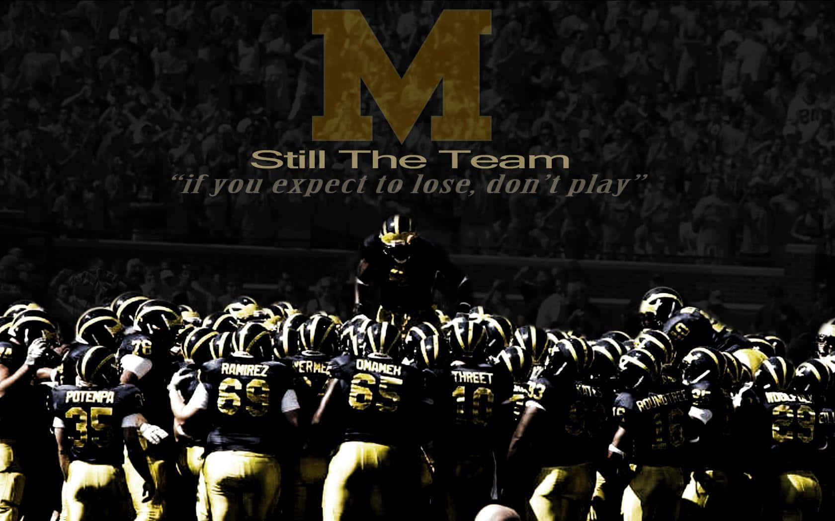 Michigan Football 桌布 壁紙 — 一支穿著黑色和金色制服的美式足球隊在一個大型「M」標誌下聚集，上方有激勵文字。