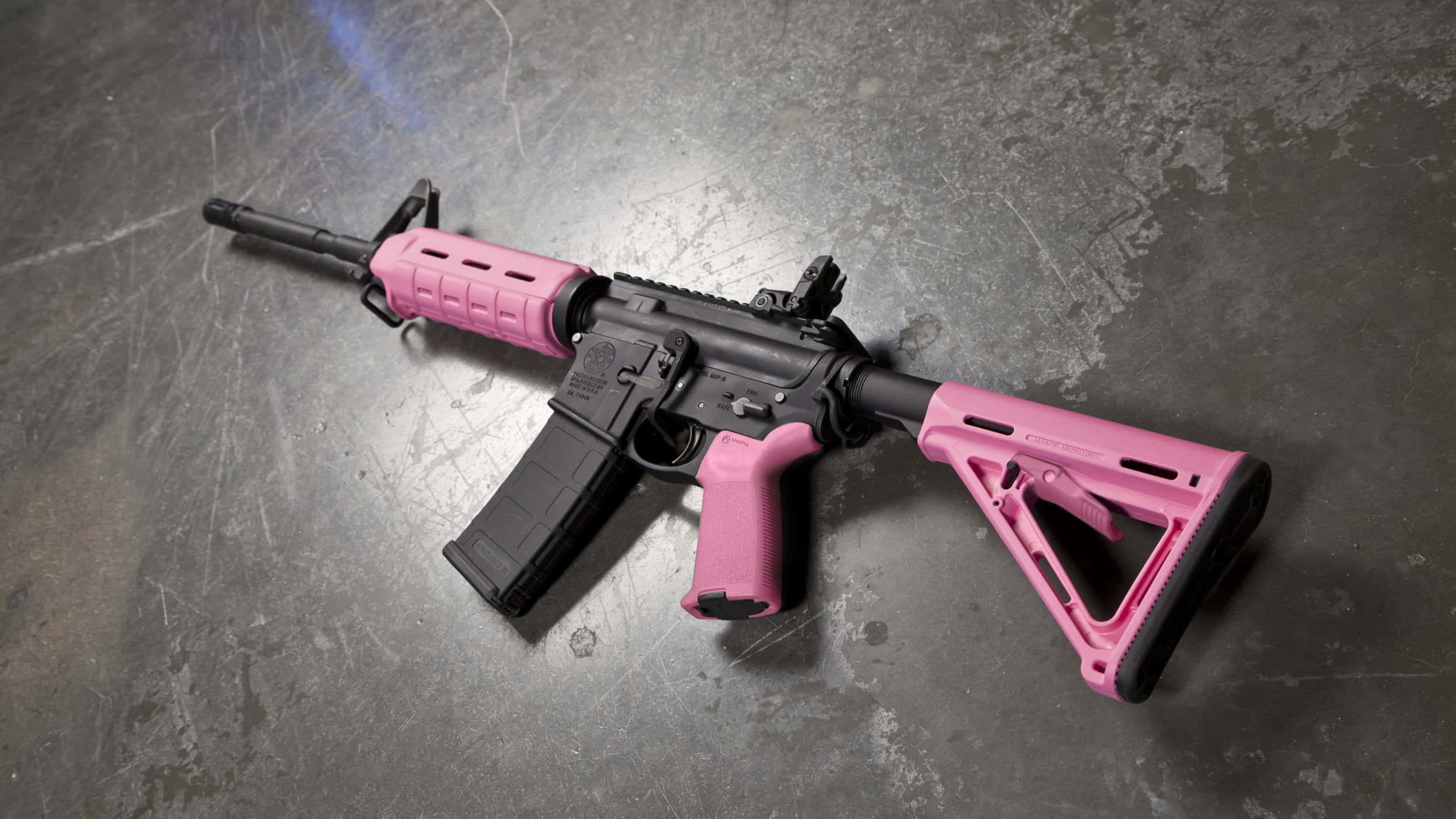 Rifle 桌布 壁紙 — 一支粉紅色和黑色的步槍在聚焦照明下放在有刮痕的金屬表面上。