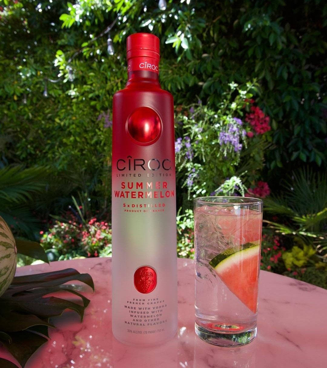 飲料 桌布 壁紙 — 一支紅色Ciroc Summer Watermelon伏特加酒瓶放在戶外粉紅色大理石桌上，旁邊有一杯西瓜雞尾酒。