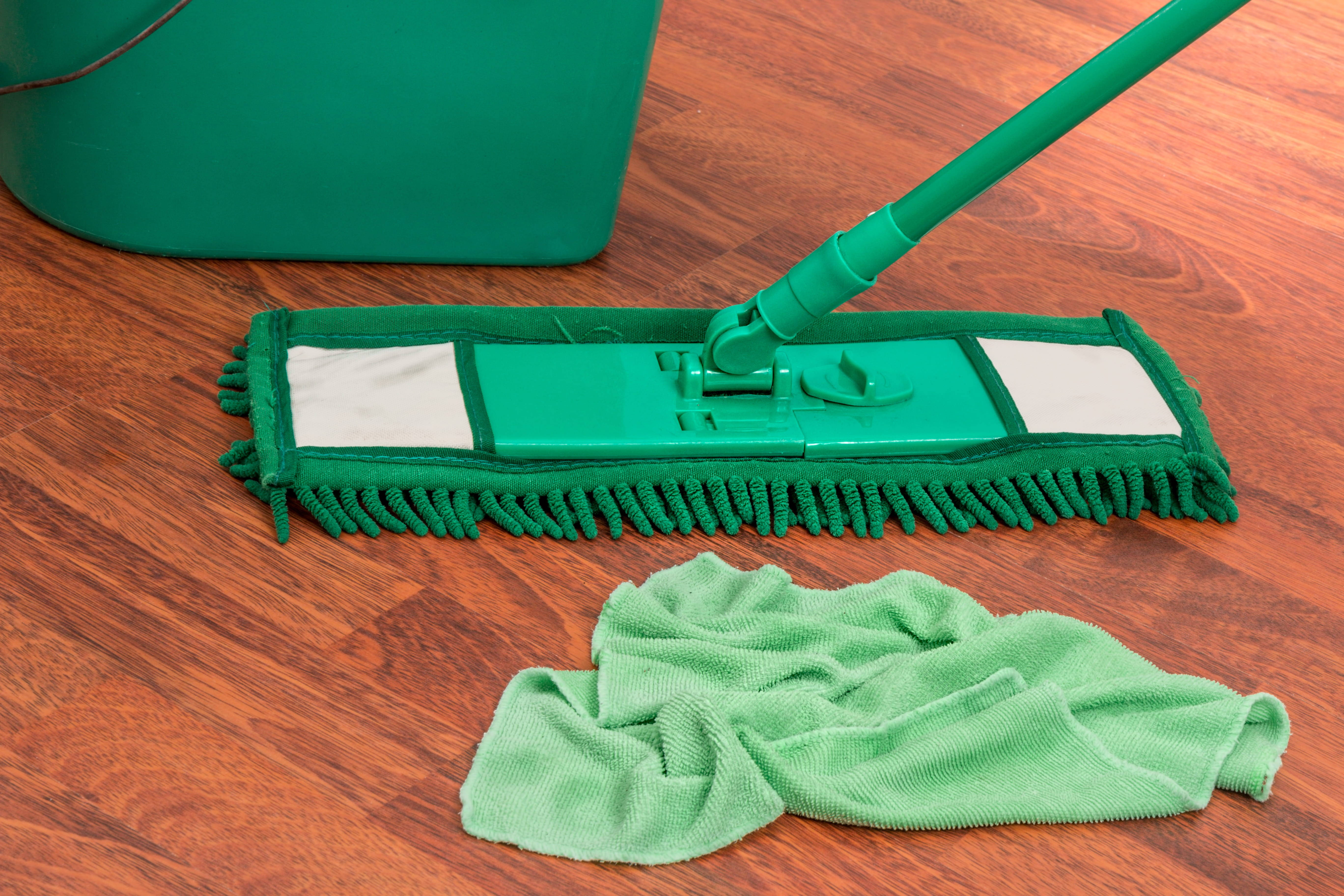 Cleaning 桌布 壁紙 — 一支綠色超細纖維拖把和相配的布塊放在拋光木地板上，旁邊有一個綠色水桶。