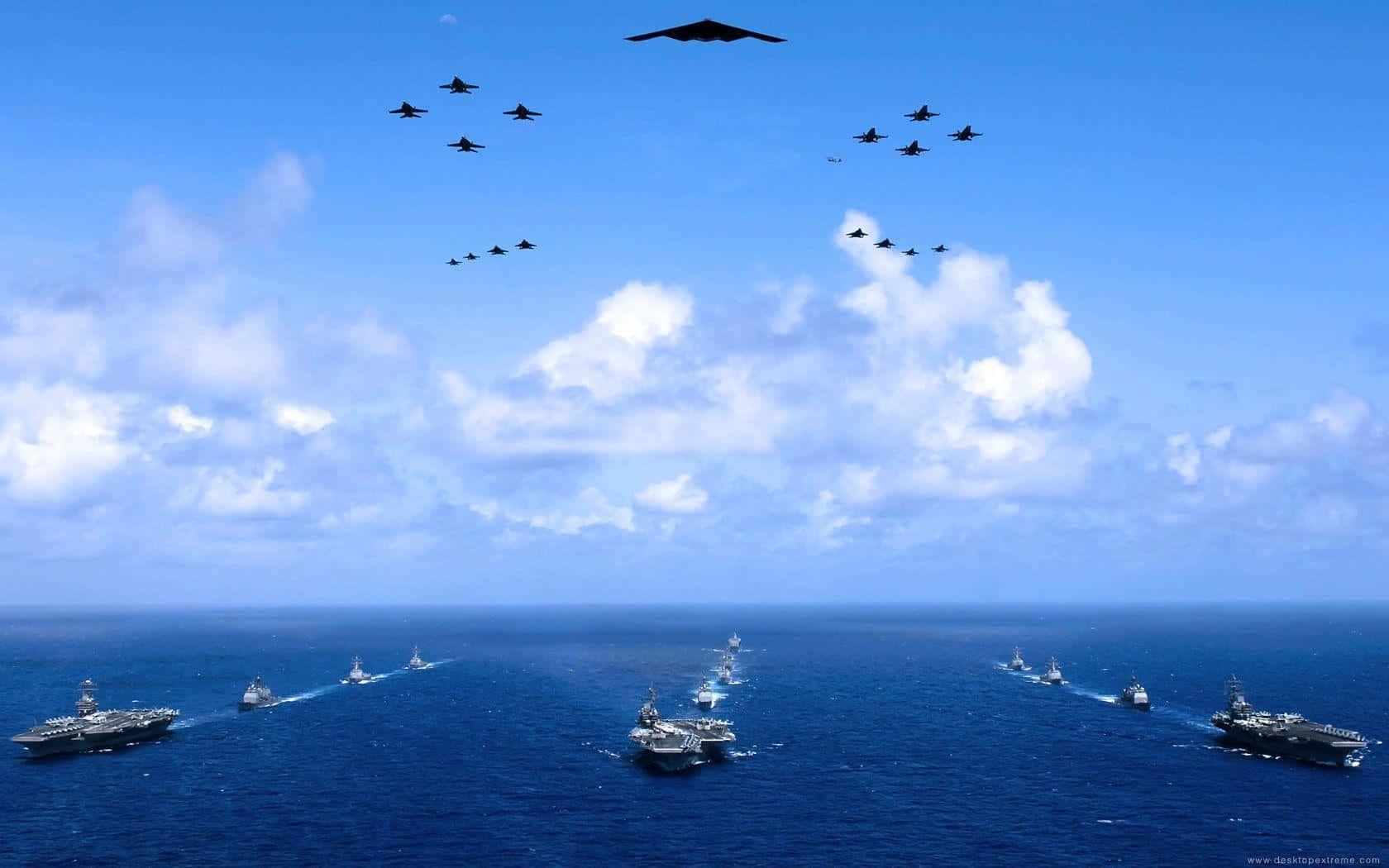 Navy 桌布 壁紙 — 一支航空母艦和戰鬥機艦隊在晴朗的天空下，飄浮著 fluffy 白色雲朵，飛越廣闊的藍色海洋。