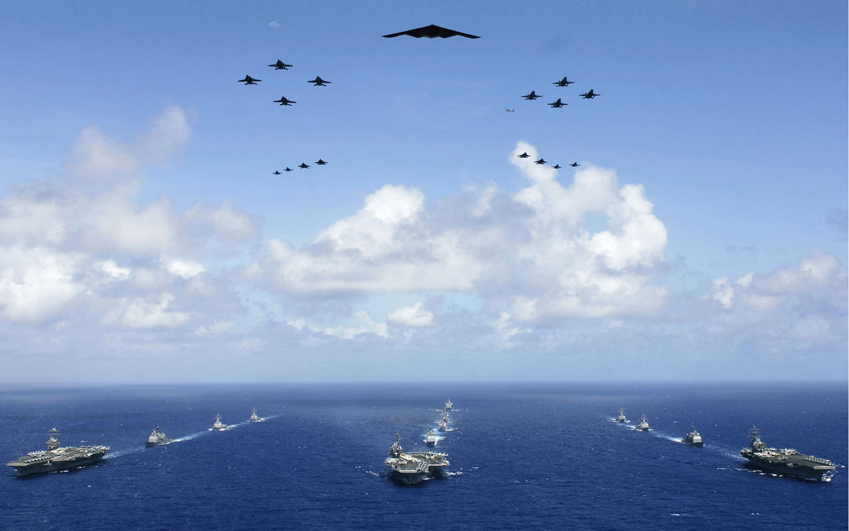 Warship 桌布 壁紙 — 一支航空母艦和戰鬥機艦隊在部分多雲的天空下翱翔於廣闊的藍色海洋之上。