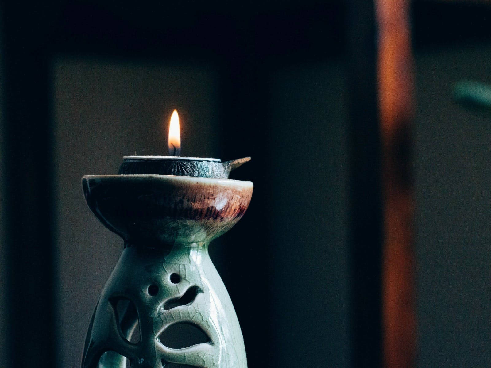 Holistic 桌布 壁紙 — 一支蠟燭在帶有雕刻葉紋的陶瓷燭台中溫暖地閃爍，背景是黑暗模糊的。