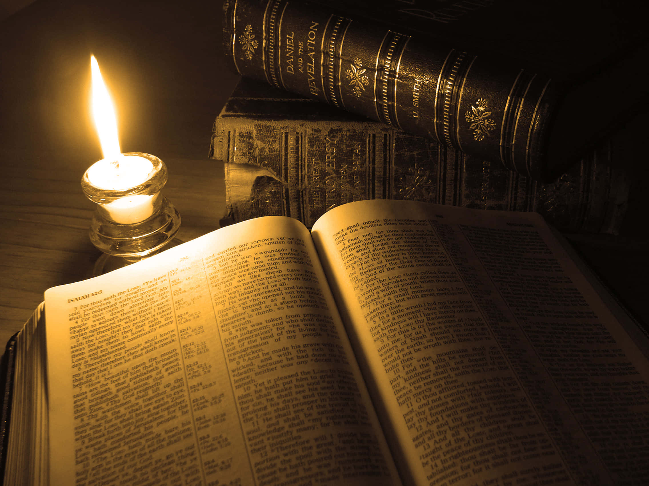 Biblical 桌布 壁紙 — 一支蠟燭在昏暗光線中溫暖地閃爍，旁邊放著一本打開的聖經，後面堆疊著裝飾精美的皮面書卷。