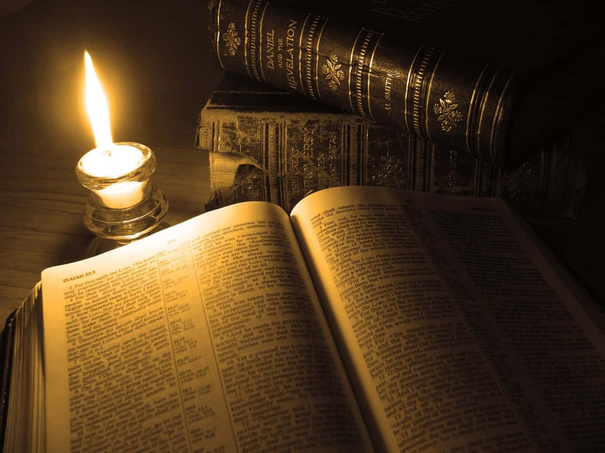 Scripture 桌布 壁紙 — 一支蠟燭溫暖地發光，旁邊放著一本打開的聖經，後面堆疊著華麗的皮面精裝書，光線昏暗。