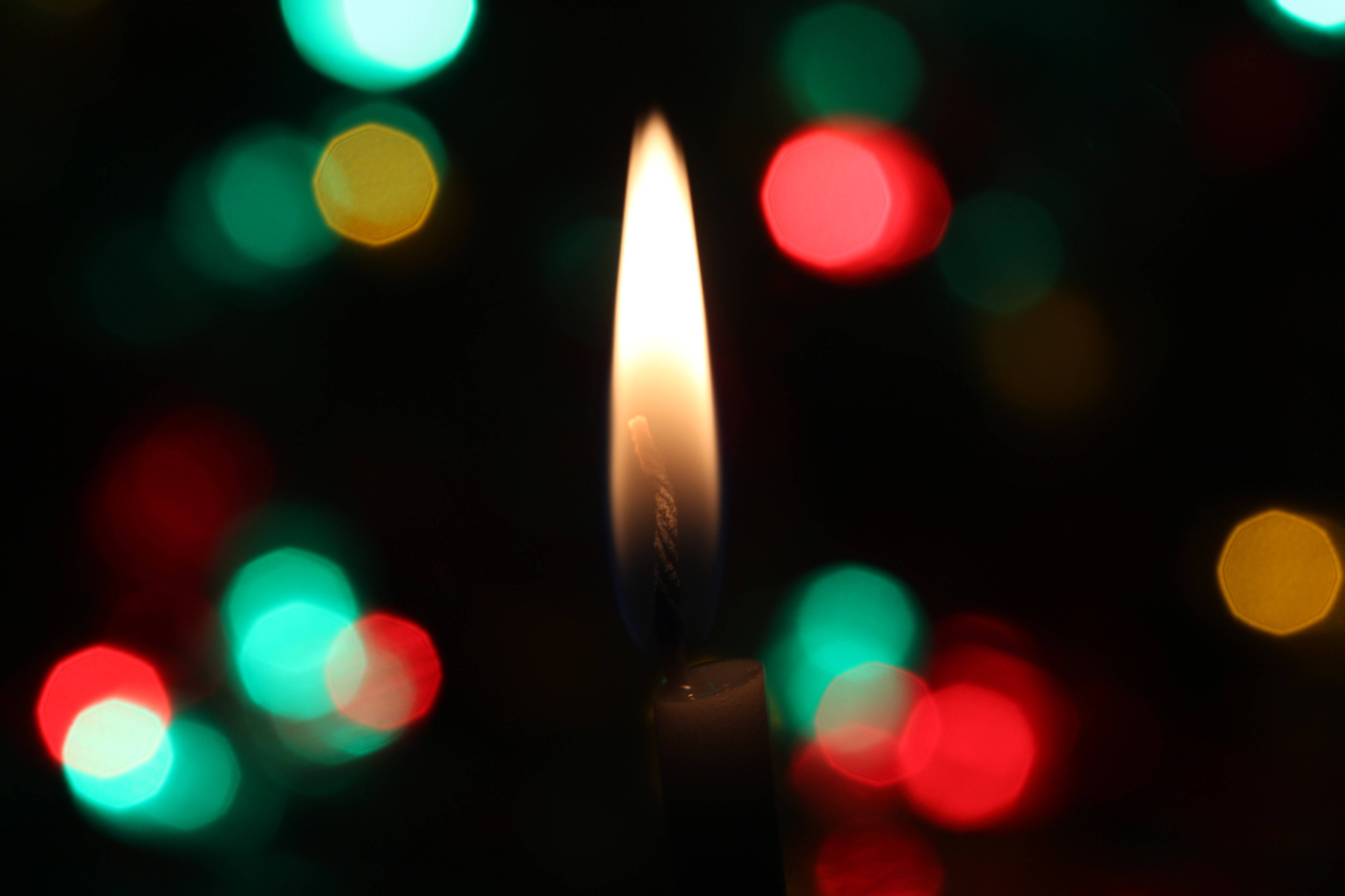 Bokeh 桌布 壁紙 — 一支蠟燭的火焰在色彩繽紛的散景燈光背景下明亮地燃燒。