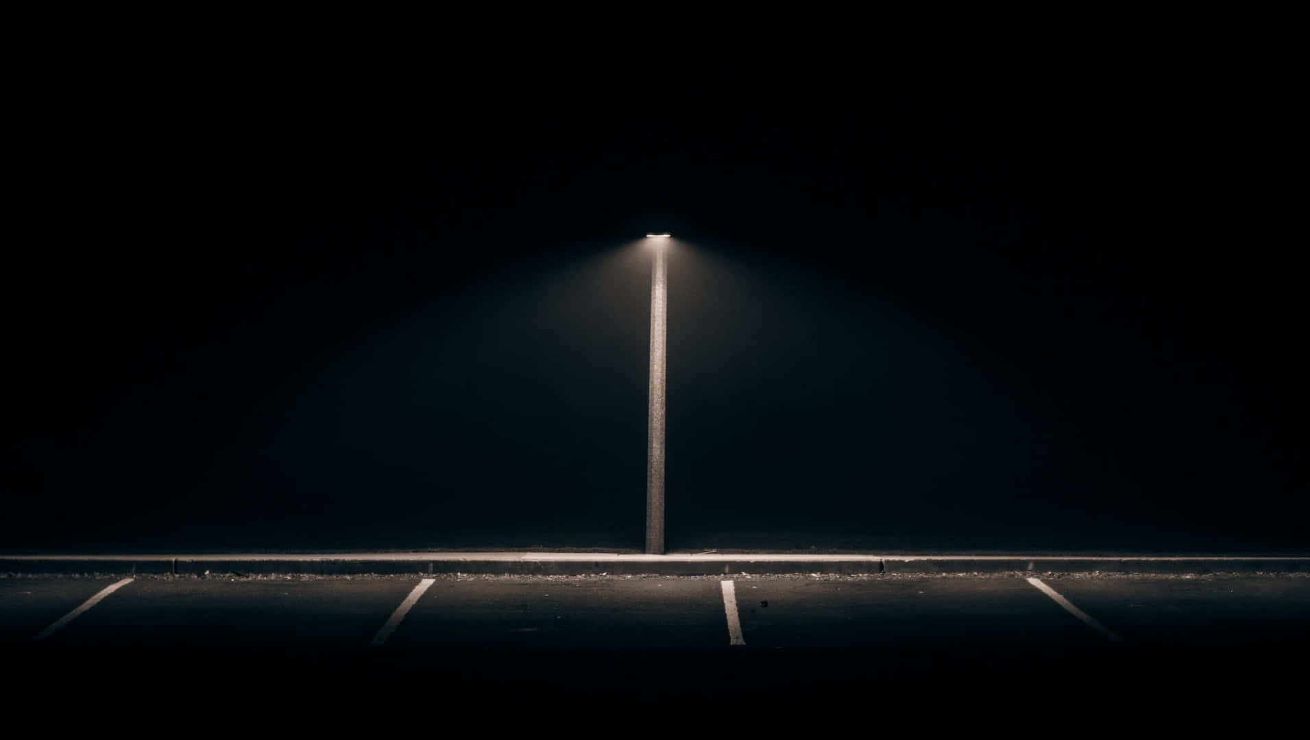 empty 桌布 壁紙 — 一支路燈在夜晚將一道強烈的光束投射在空蕩蕩的停車場上，照亮了深黑背景中褪色的白線。