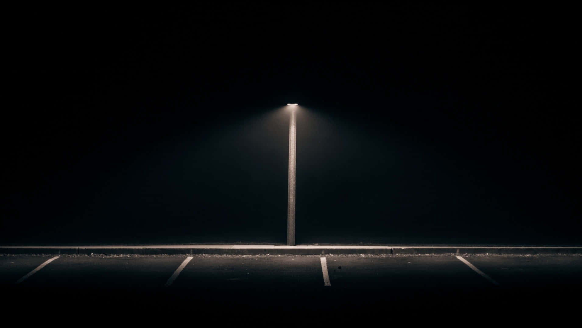 Dark Road 桌布 壁紙 — 一支路燈在漆黑一片的夜晚場景中，將一道狹窄的光束投射在空蕩蕩的停車位上。