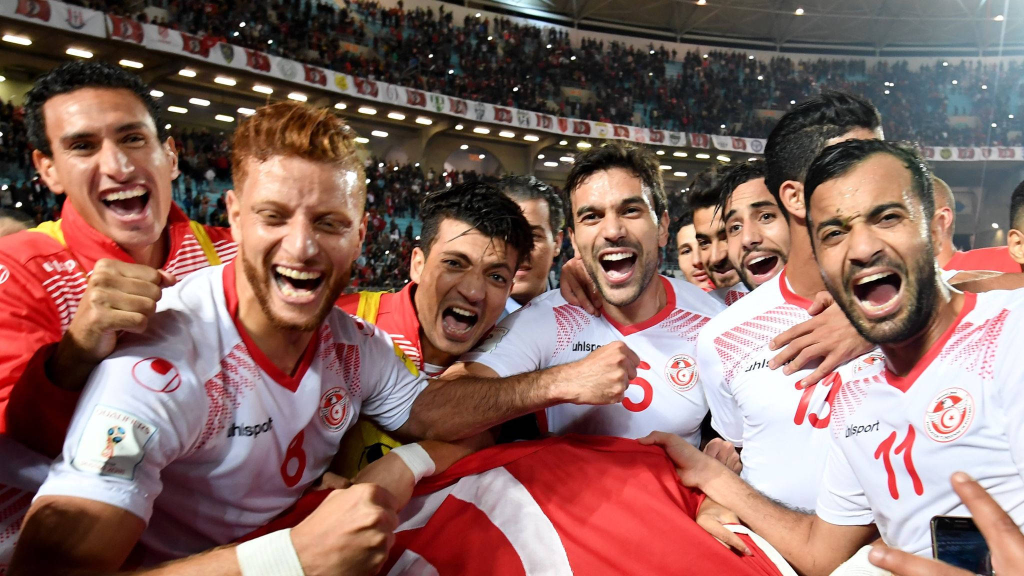 Tunisia 桌布 壁紙 — 一支身穿白色球衣的歡騰足球隊，在座無虛席的體育場中，揮舞著紅白旗幟，慶祝勝利。
