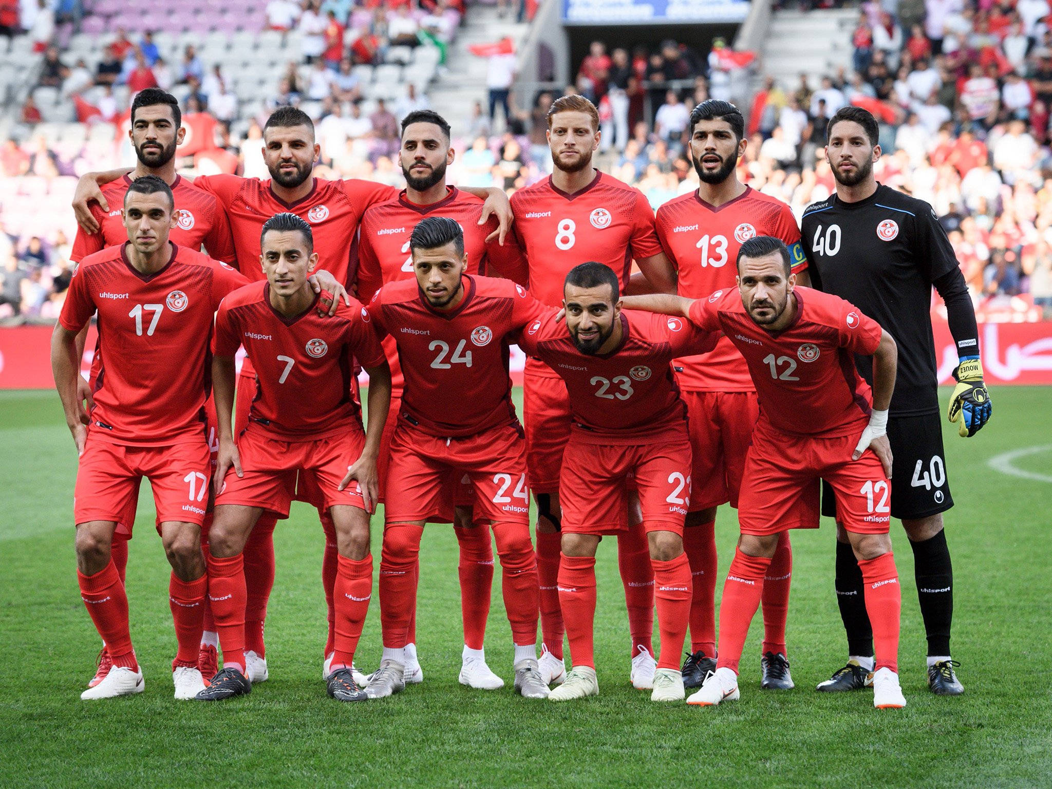 Tunisia 桌布 壁紙 — 一支身穿紅色球衣的足球隊在綠色球場上，以觀眾為背景拍攝團體照。