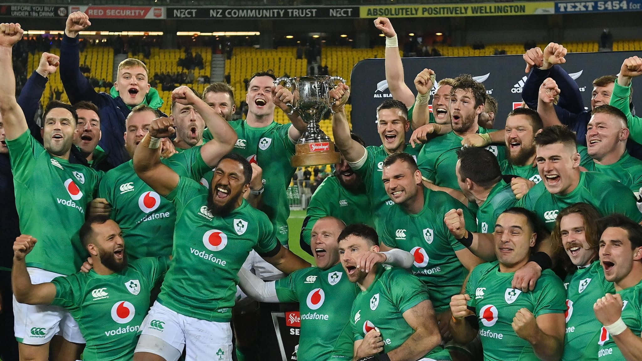 Ireland Rugby 桌布 壁紙 — 一支身穿綠色球衣的歡騰橄欖球隊在體育館內高舉閃亮的獎盃，拳頭高舉慶祝勝利。