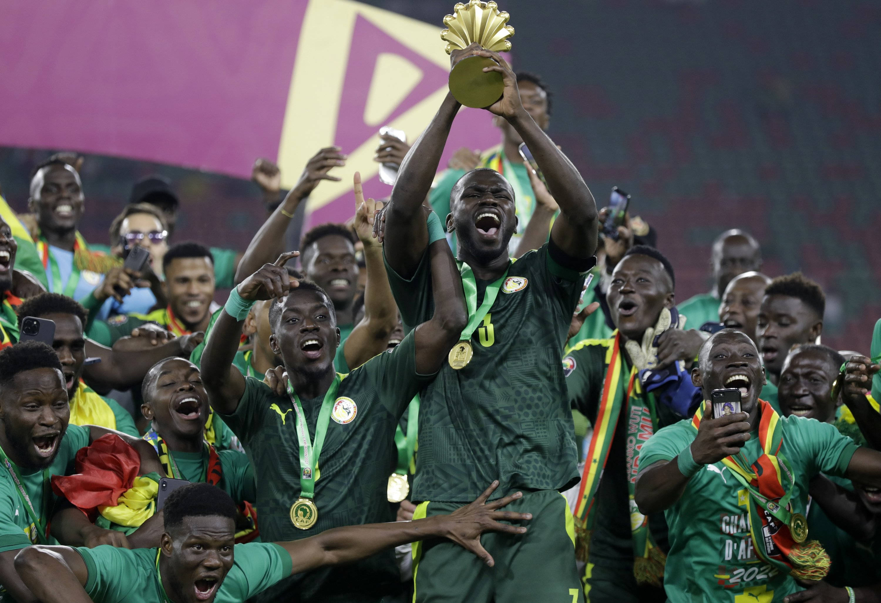 Senegal 桌布 壁紙 — 一支身穿綠色球衣的歡騰足球隊，在隊友歡呼慶祝勝利的同時，將金色獎盃高舉過頭，球場燈光下氣氛熱烈。