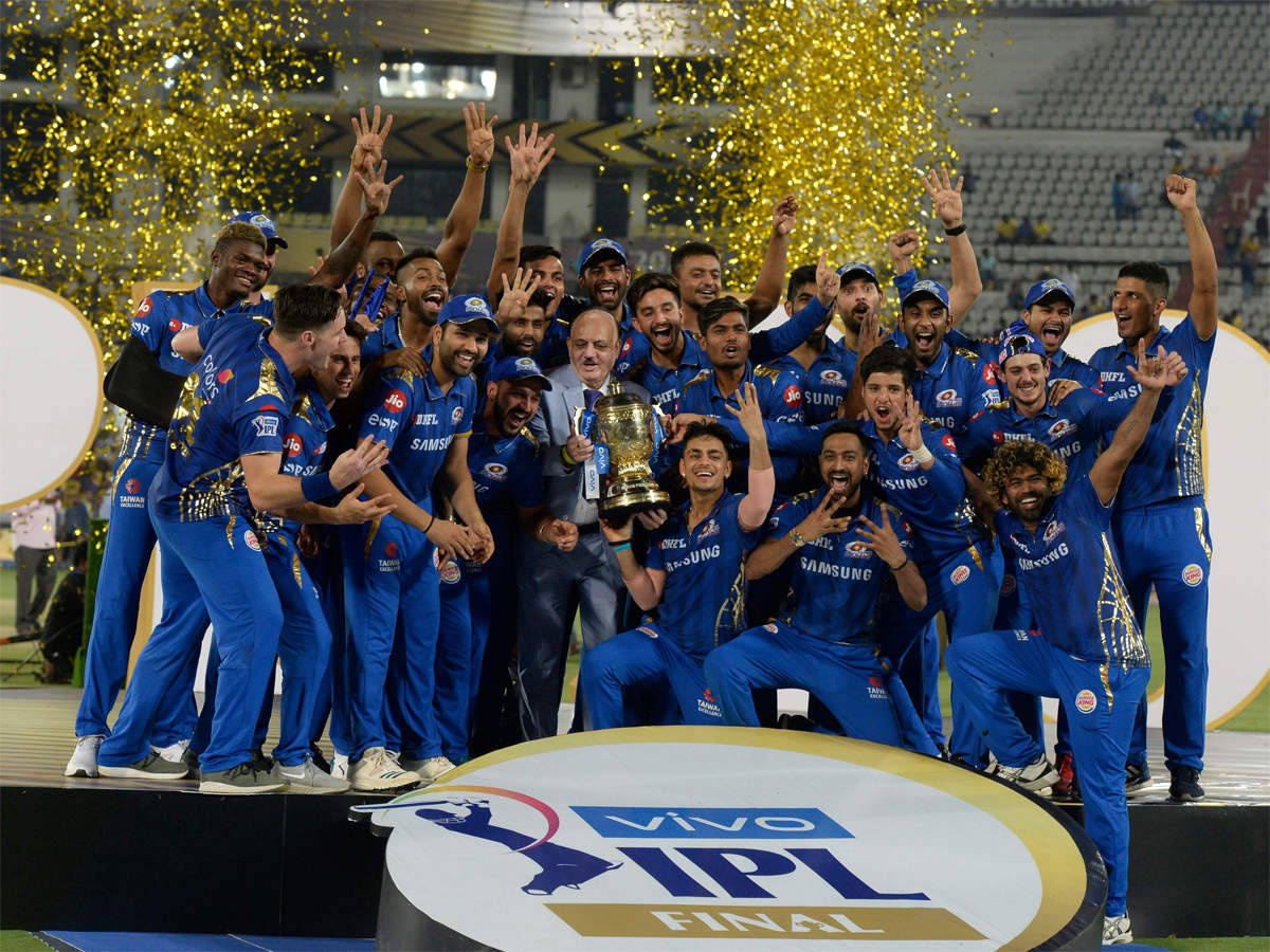 Mumbai Indians 桌布 壁紙 — 一支身穿藍色隊服的板球隊在頒獎台上慶祝勝利，金色紙屑在他們周圍飄落，他們高舉獎盃。