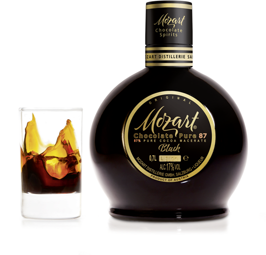 飲料 桌布 壁紙 — 一支閃亮的Mozart Chocolate Pure 87 Black利口酒瓶立在一個裝有旋轉琥珀色液體的玻璃杯旁，背景是純白色。