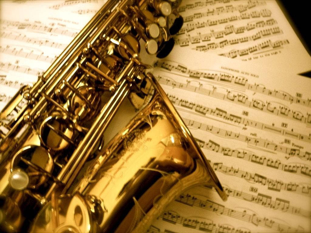 Beautiful Music 桌布 壁紙 — 一支閃亮金色薩克斯風斜放在樂譜上，帶有溫暖的懷舊色調和柔和陰影。