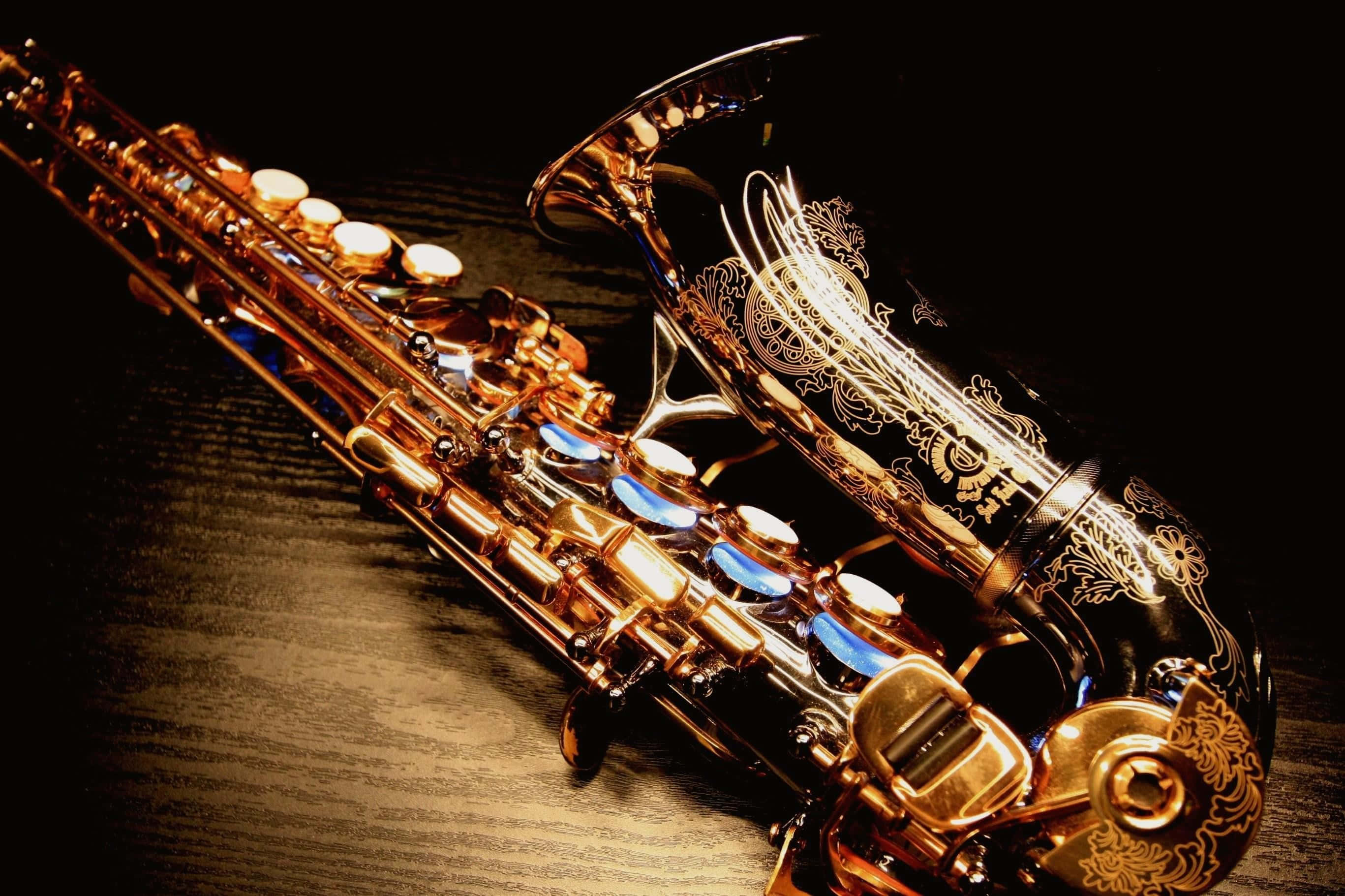 Jazz 桌布 壁紙 — 一支閃閃發光的金色薩克斯風，帶有精細雕刻，在戲劇性燈光下斜放在深色木質表面上。