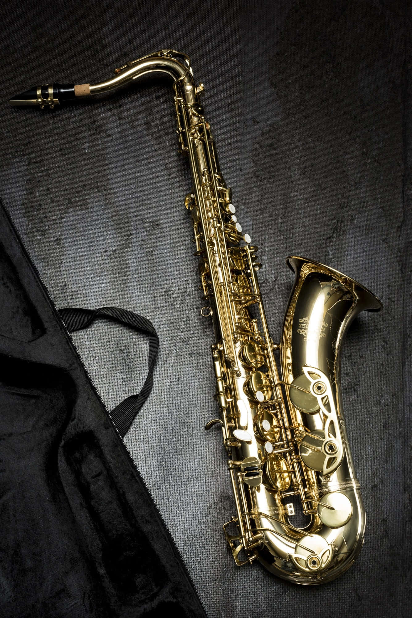 Musical Instrument 桌布 壁紙 — 一支閃閃發光的金色薩克斯風斜放在深色紋理表面上，旁邊是其黑色琴盒。