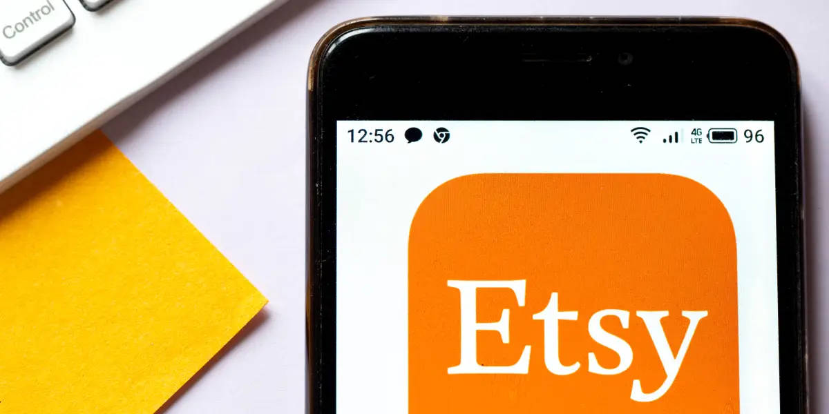 etsy 桌布 壁紙 — 一支顯示 Etsy 應用程式標誌的智慧型手機放在白色桌子上，旁邊有一張黃色便利貼和鍵盤。
