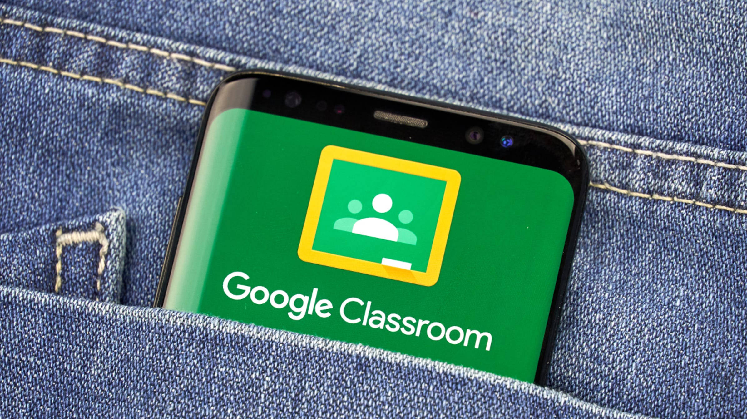 Learning 桌布 壁紙 — 一支顯示 Google Classroom 應用程式的智慧型手機從藍色牛仔褲口袋中探出頭來。