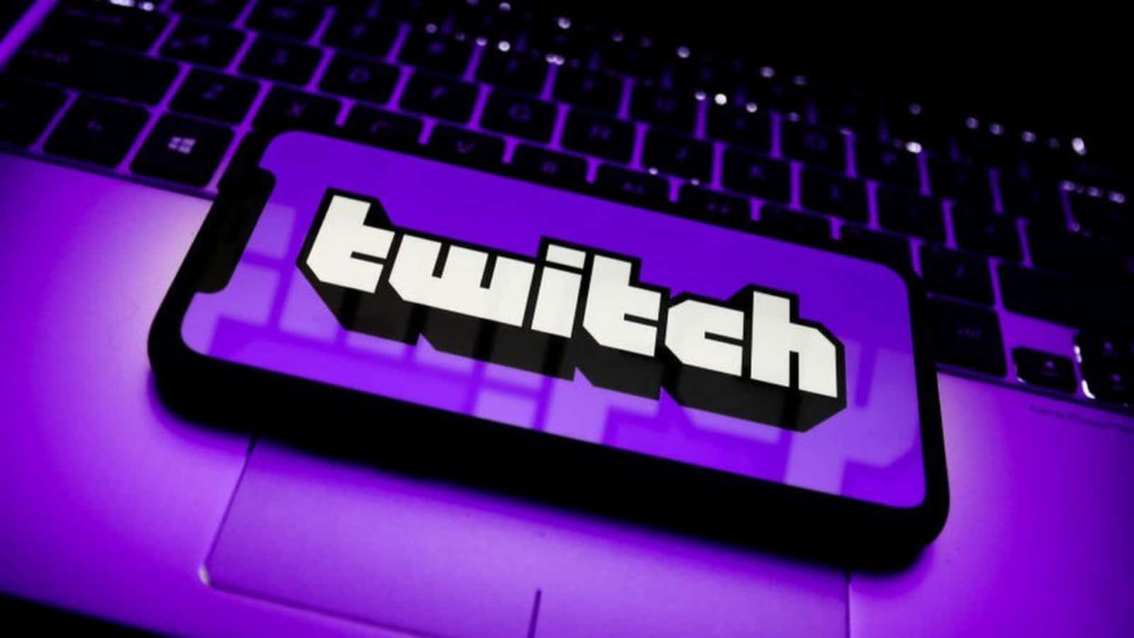 Twitch 桌布 壁紙 — 一支顯示 Twitch 標誌的智慧型手機放在被鮮豔紫色燈光籠罩的筆記型電腦鍵盤上。