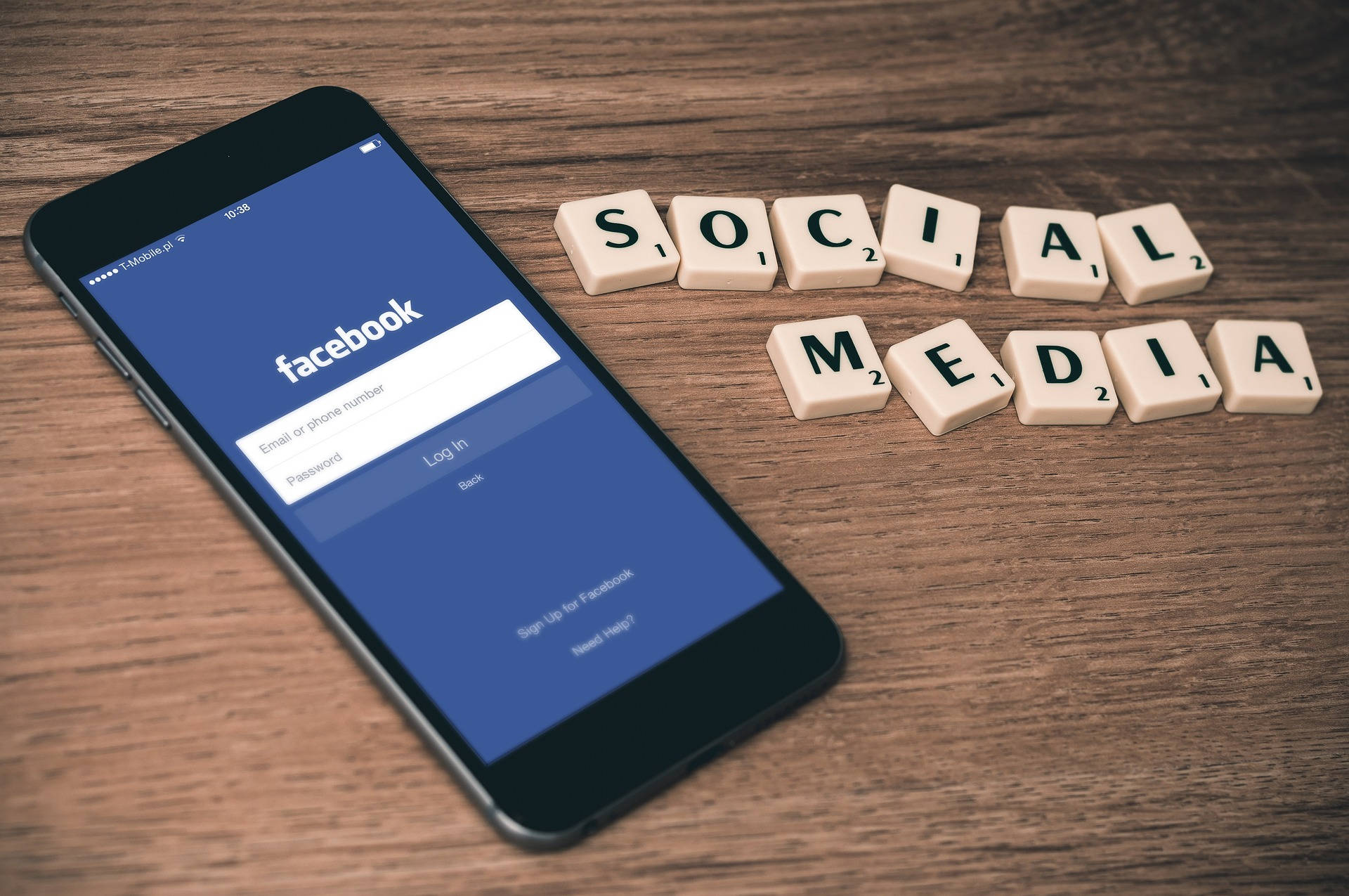 科技動圖 桌布 壁紙 — 一支顯示Facebook登入畫面的智慧型手機，旁邊放著拼出「SOCIAL MEDIA」的Scrabble字母磚，在木桌上。