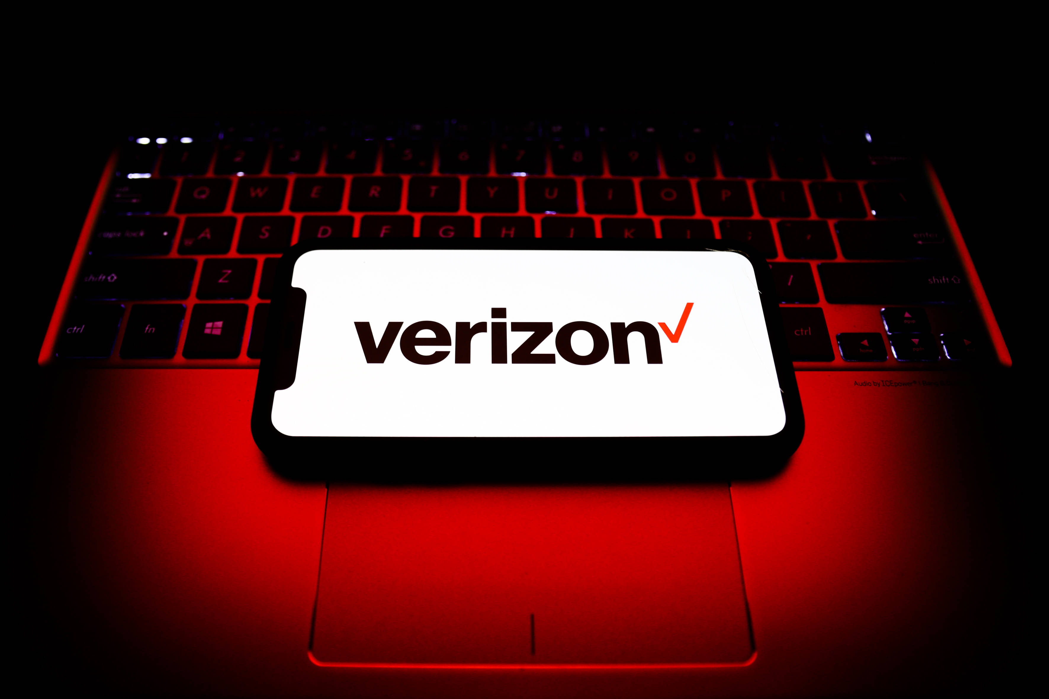 Verizon 桌布 壁紙 — 一支顯示Verizon標誌的智慧型手機放在一個被強烈紅色背光照亮的筆記型電腦鍵盤上，背景為深色。