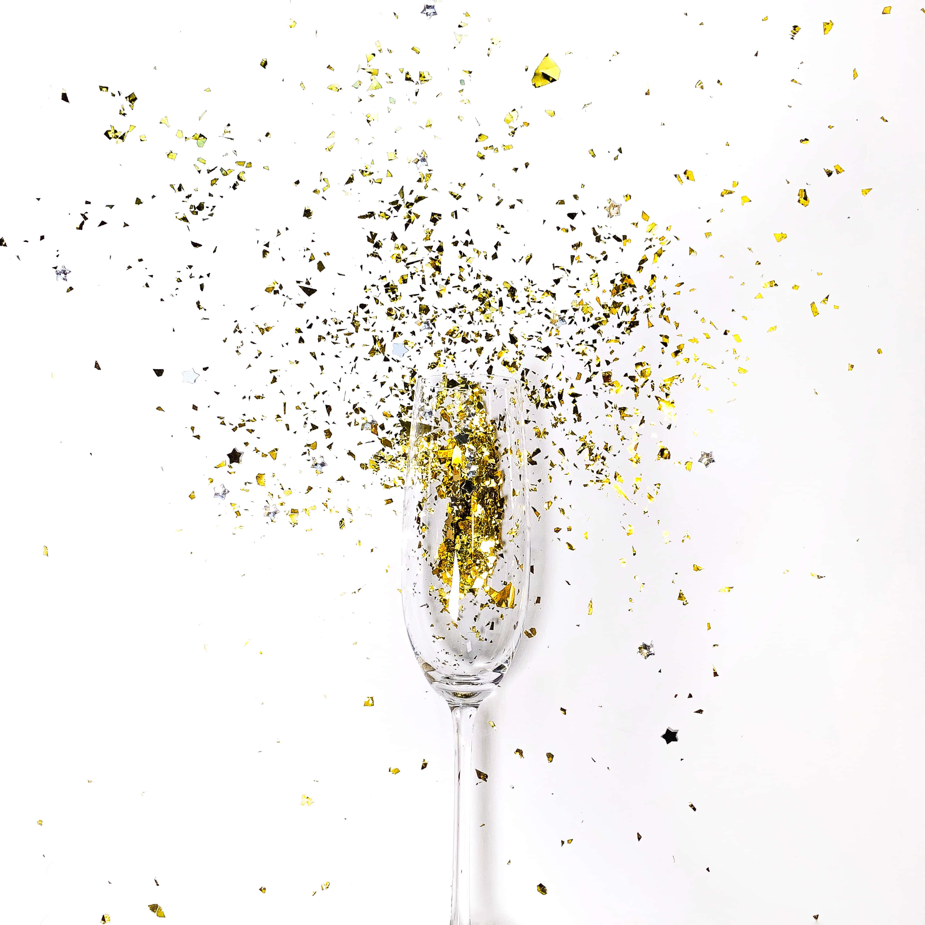 Gold Confetti 桌布 壁紙 — 一支香檳杯在純白背景上爆出金色紙屑，營造出節日慶祝的時刻。