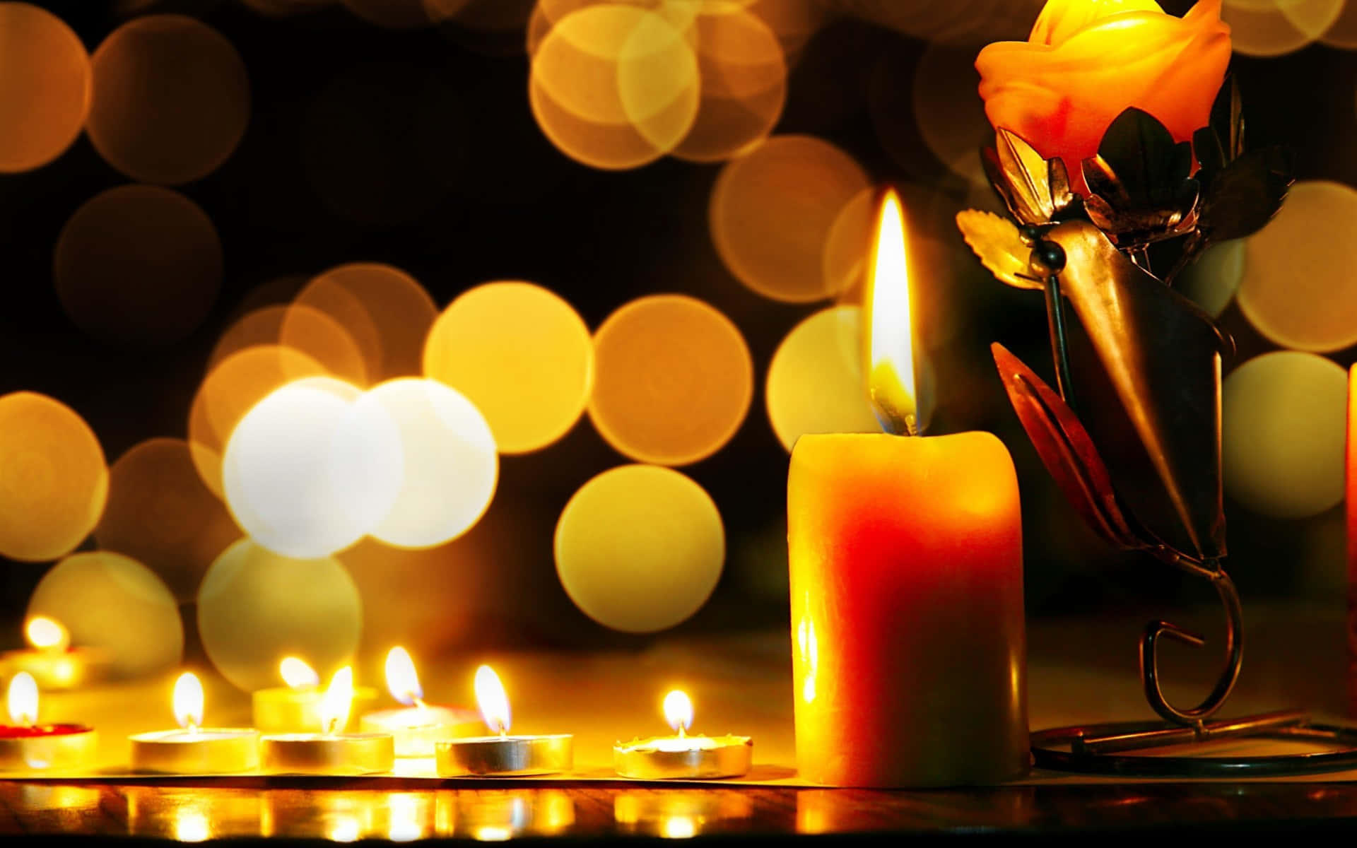 Candle Light 桌布 壁紙 — 一支高大的蠟燭和小茶燈在金屬燭台上的玫瑰旁邊，在散景背景下溫暖地發光。