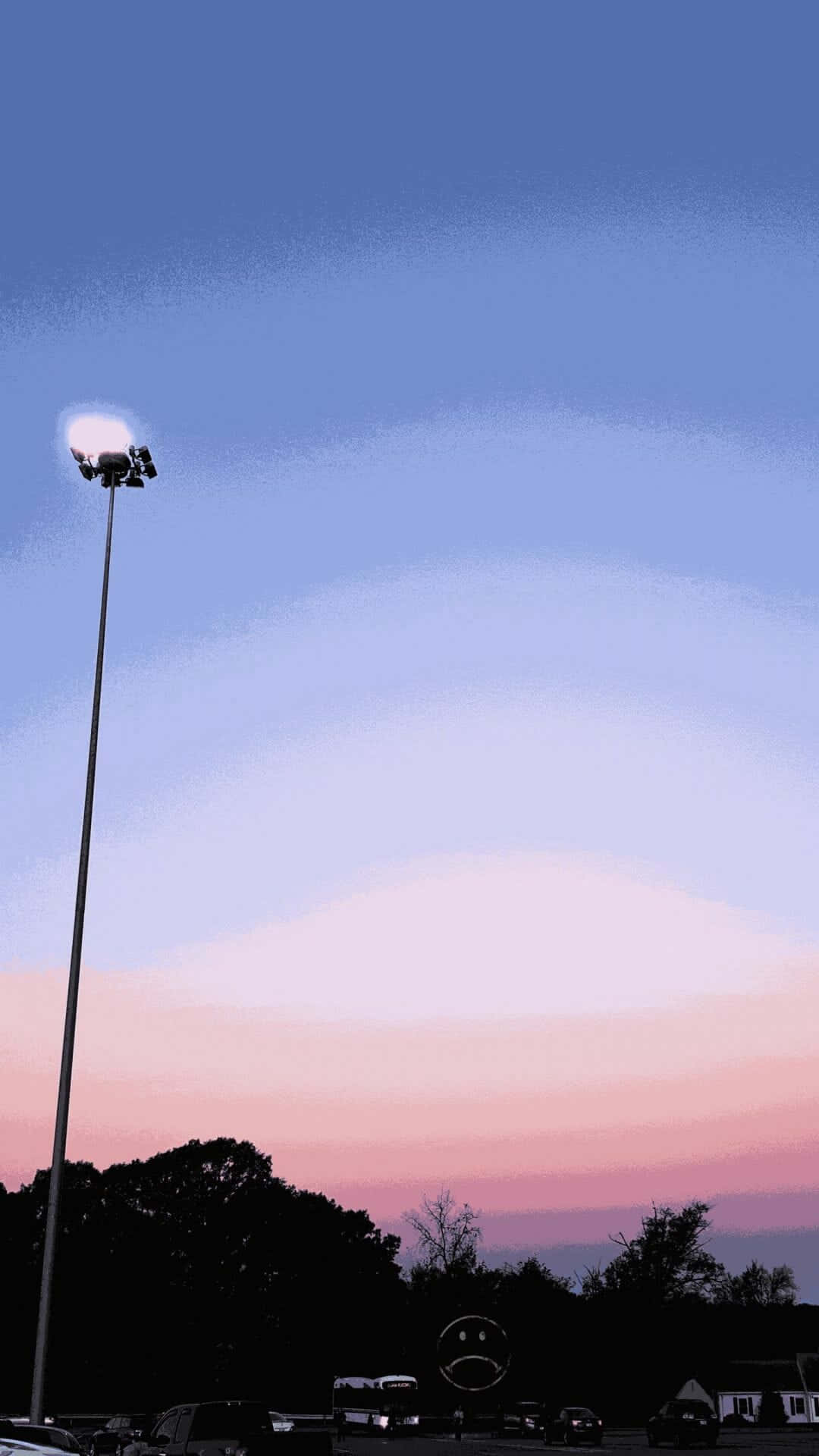 Clouds Aesthetic Tumblr 桌布 壁紙 — 一支高燈柱矗立在停車場上方，背景是柔和的粉紅和藍色調的暮色天空，樹木和汽車的剪影清晰可見。