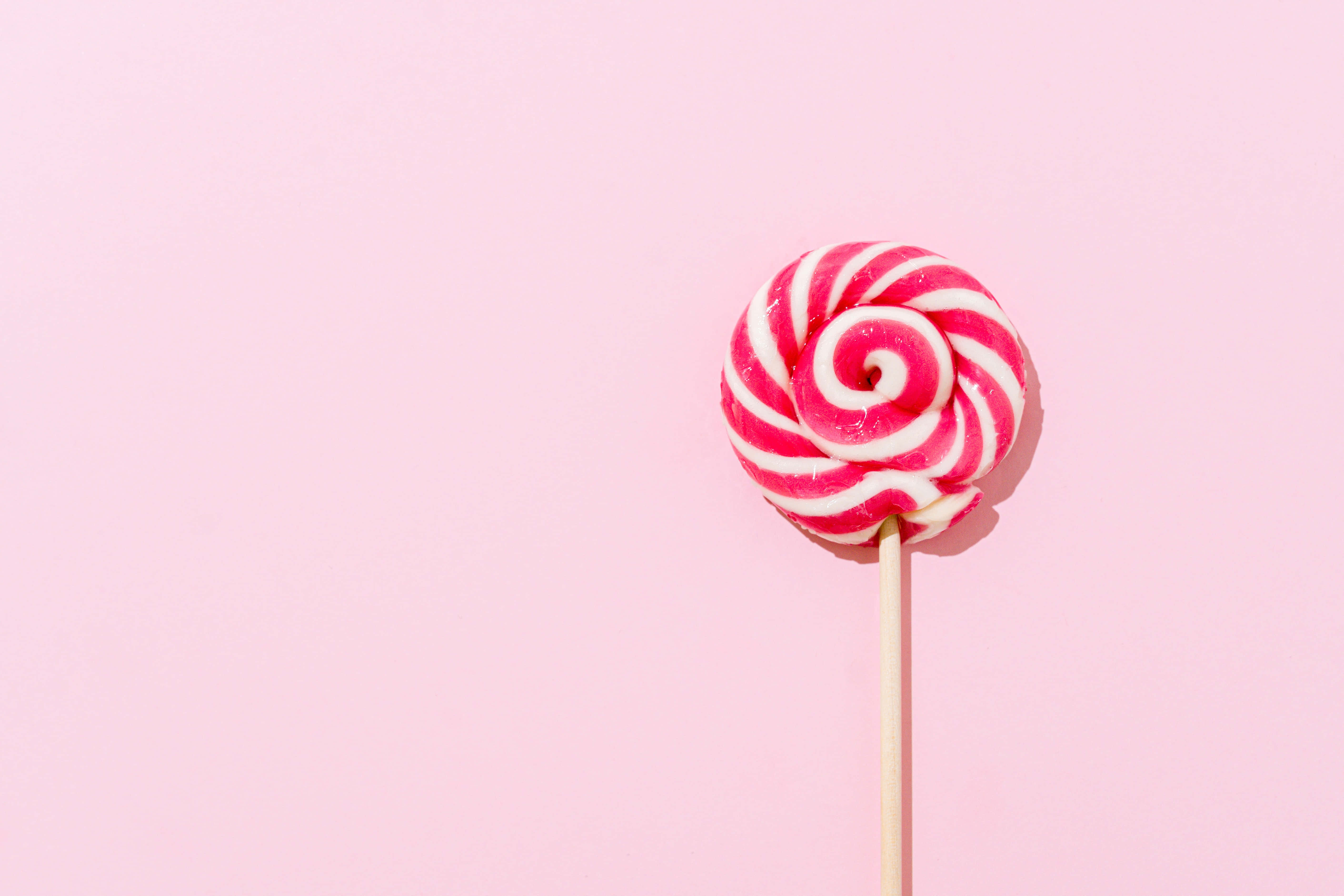 Pink Candy 桌布 壁紙 — 一支鮮豔的粉紅和白色漩渦棒棒糖單獨立在柔和的粉彩粉紅背景前。