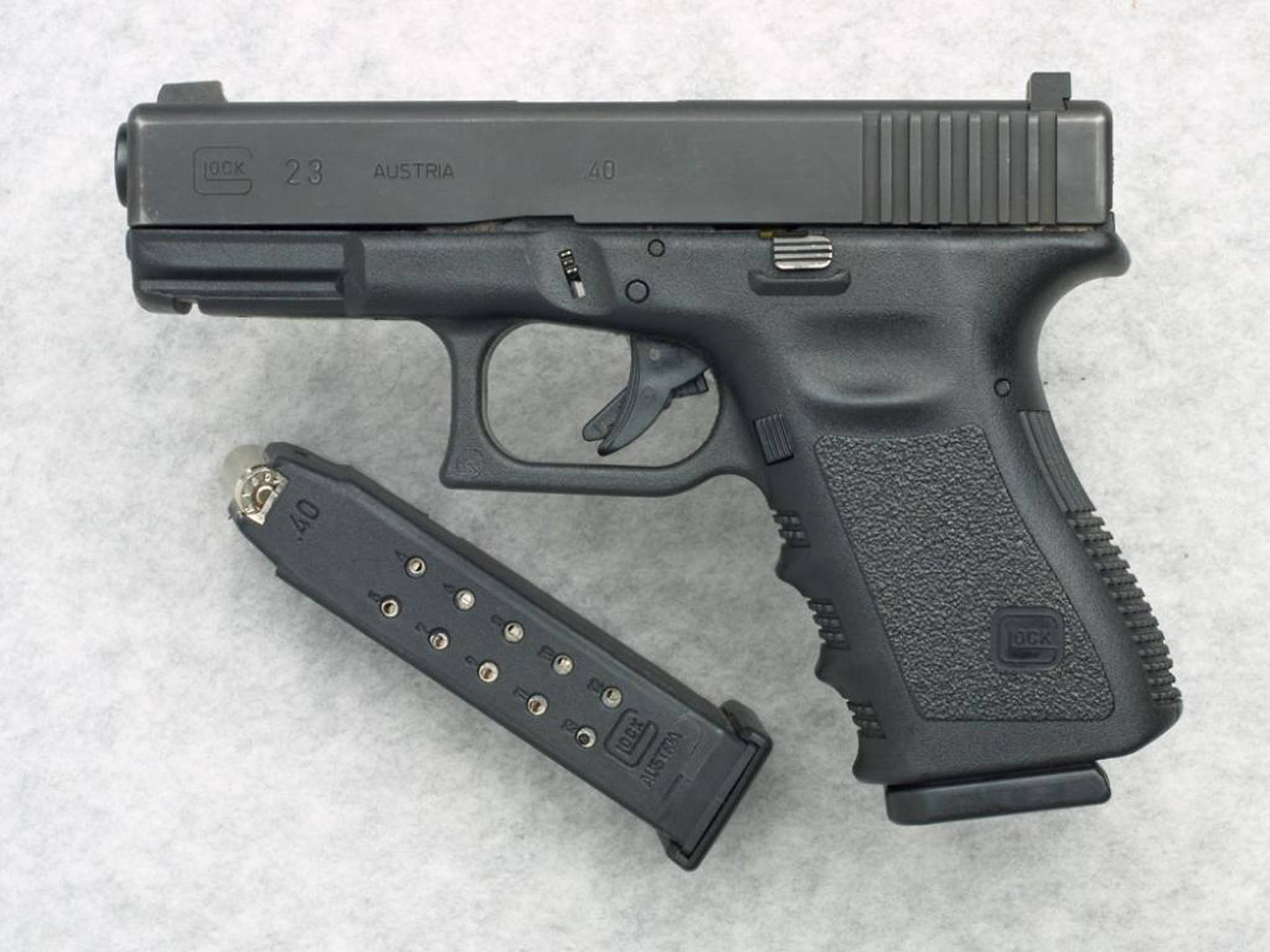 克拉克 桌布 壁紙 — 一支黑色Glock 23手槍連彈匣放在有紋理的灰色表面上，乾淨的攝影棚拍攝。