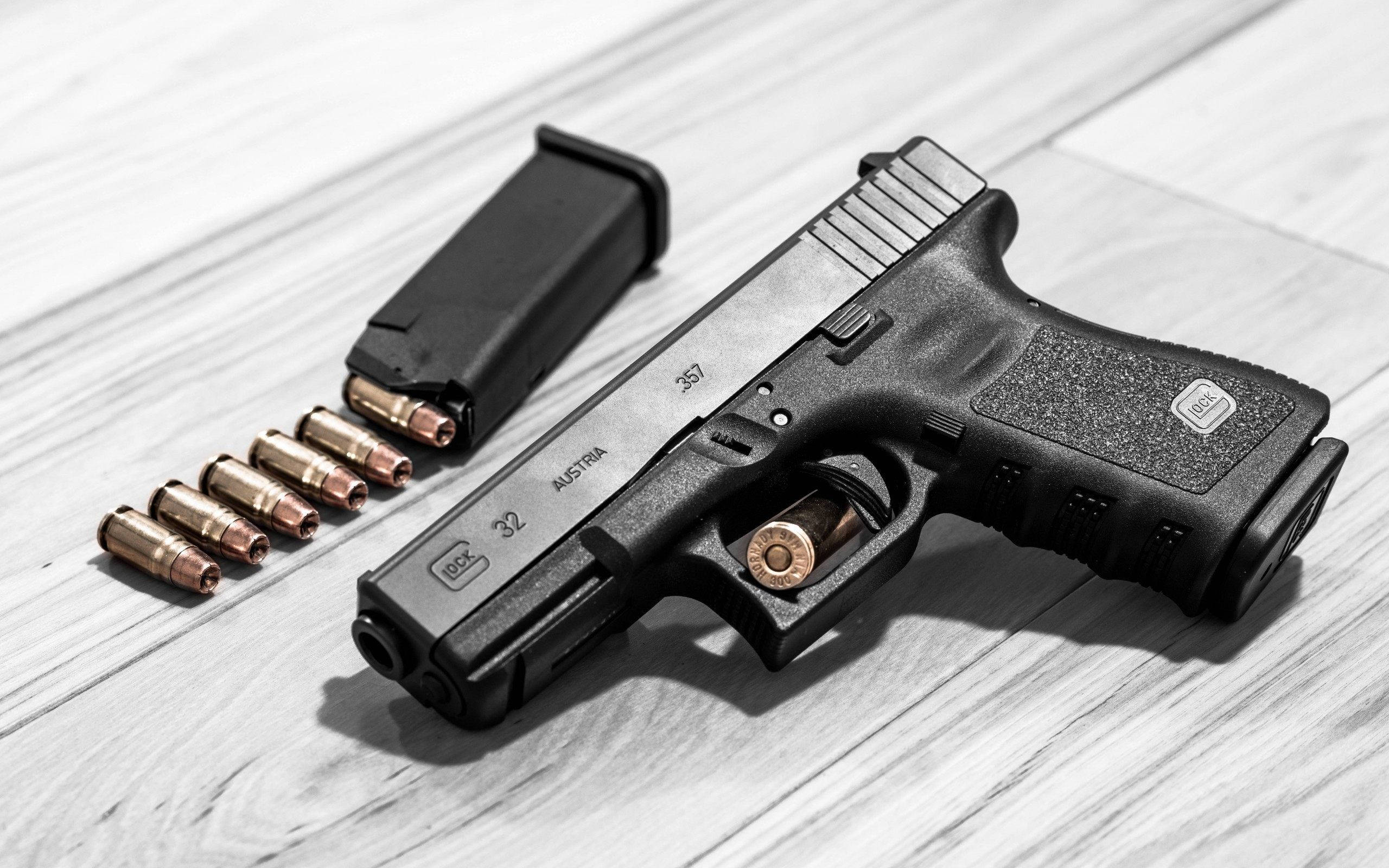 克拉克 桌布 壁紙 — 一支黑色Glock 32手槍連彈匣及子彈放在淺色木質表面上，高對比照明。