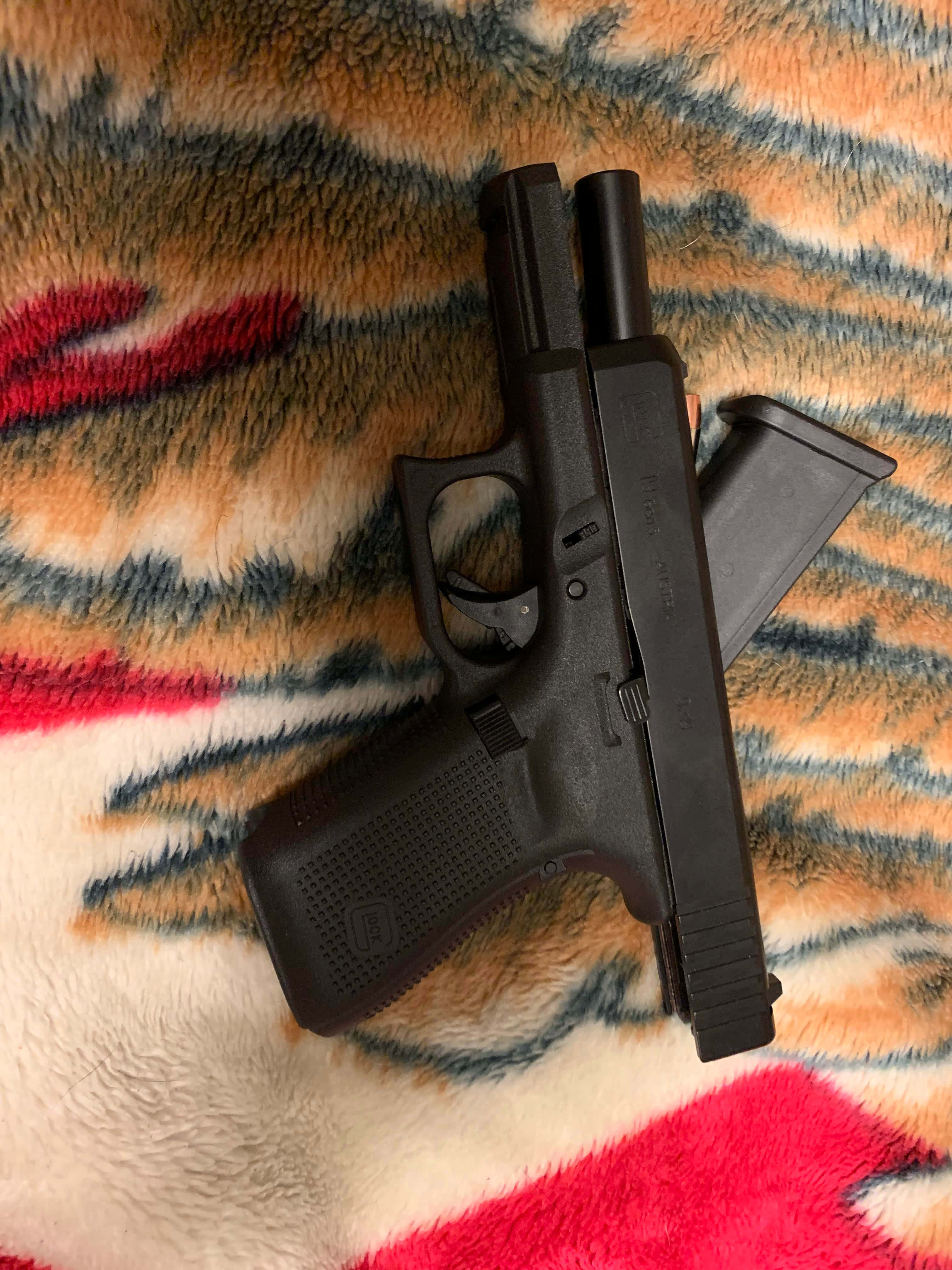 Glock 19 桌布 壁紙 — 一支黑色手槍和彈匣放在一條色彩繽紛、毛茸茸的毯子上，毯子有橙色、紅色和藍色的圖案。
