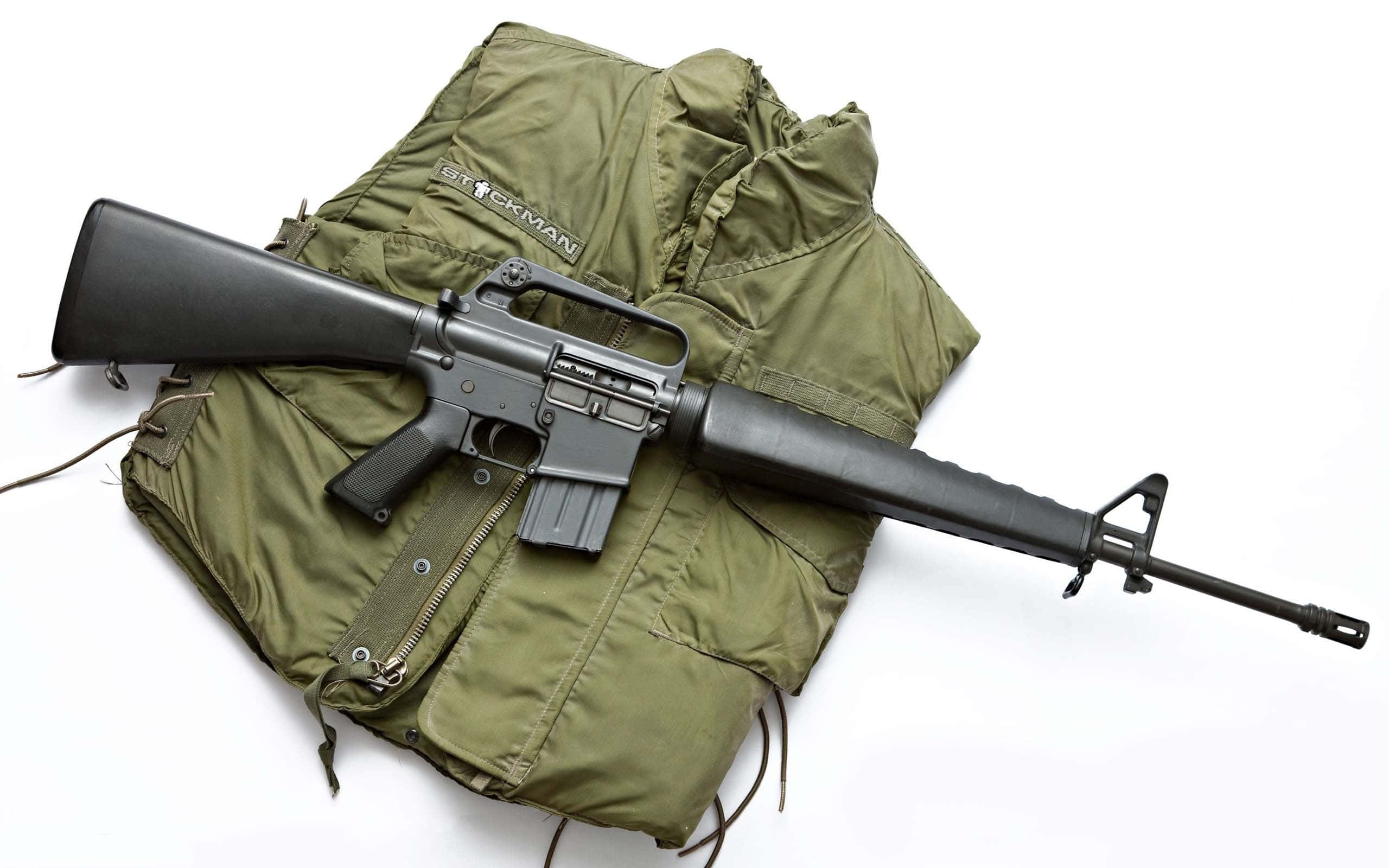 Rifle 桌布 壁紙 — 一支黑色步槍放在橄欖綠色戰術背心上，背景為純白色。