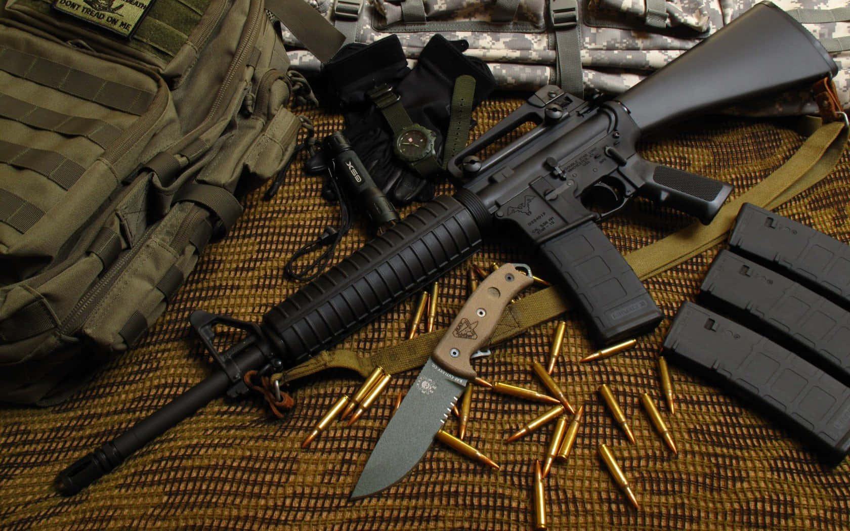 Rifle 桌布 壁紙 — 一支黑色突擊步槍和戰術裝備放在編織墊上，周圍有黃銅子彈和一把固定刀片刀。