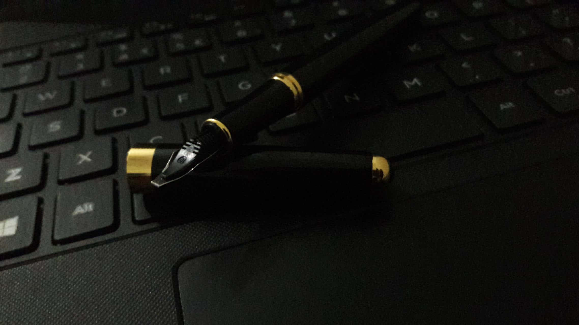 Pen 桌布 壁紙 — 一支黑色金邊鋼筆斜放在昏暗的深色筆記型電腦鍵盤上。