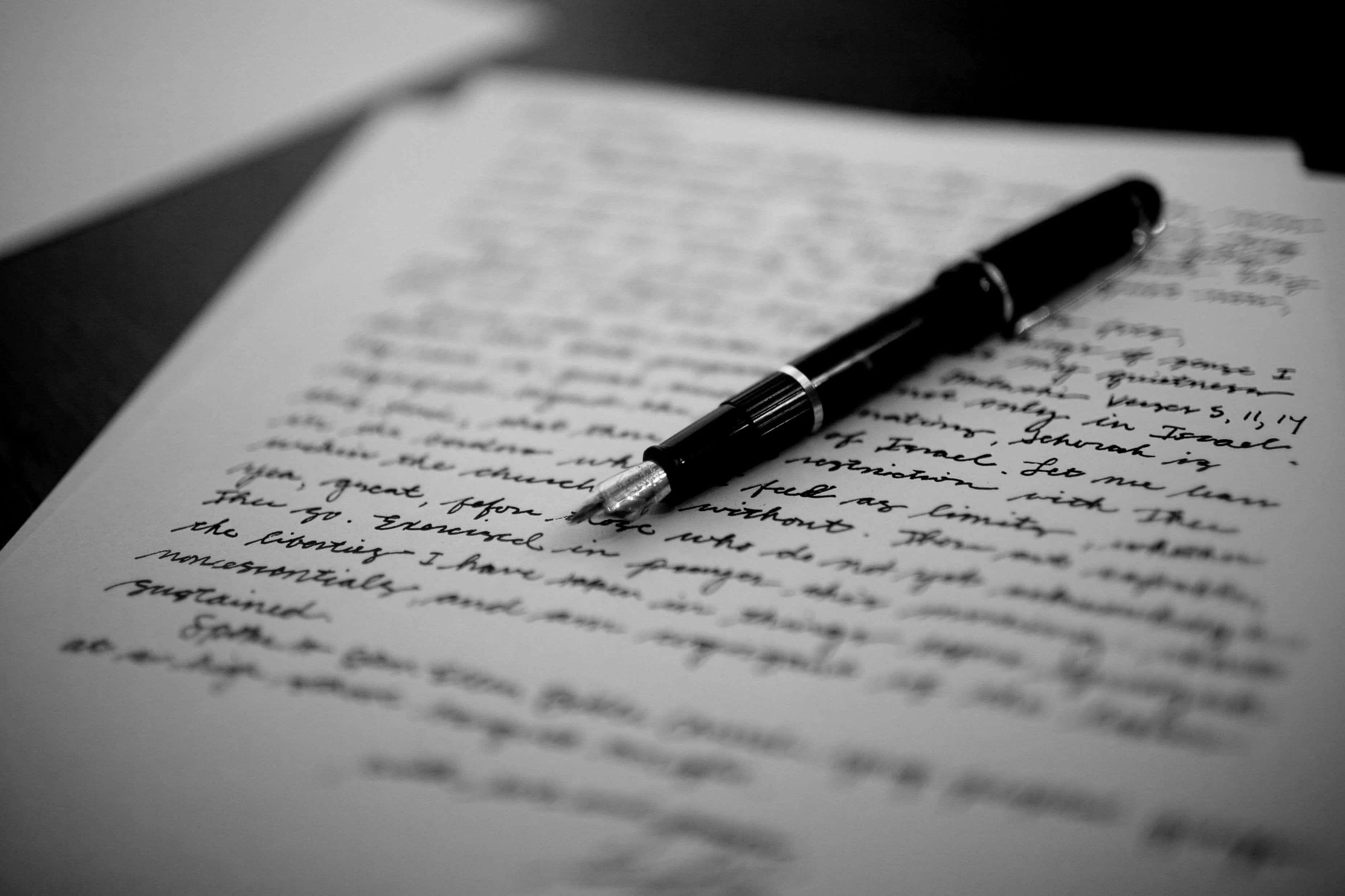 Pen 桌布 壁紙 — 一支黑色鋼筆放在手寫字頁面上，呈現淺景深黑白效果。