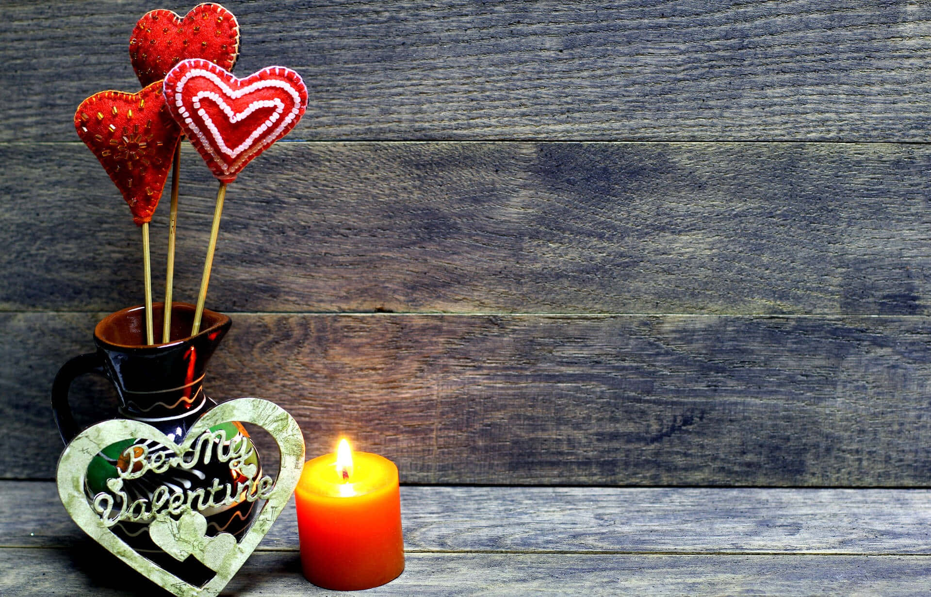 Romantic Love 桌布 壁紙 — 一支點燃的橙色蠟燭和紅色心形棒棒糖放在一個「Be My Valentine」心形相框旁邊，置於風化的木板上。