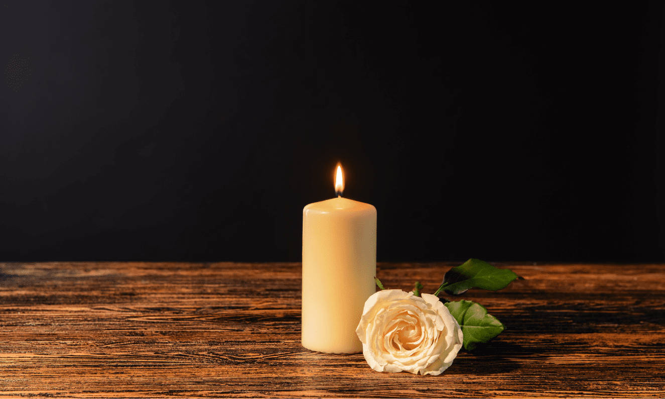 Condolence 桌布 壁紙 — 一支點燃的白色蠟燭和一朵白玫瑰放在黑色背景的深色木桌上。