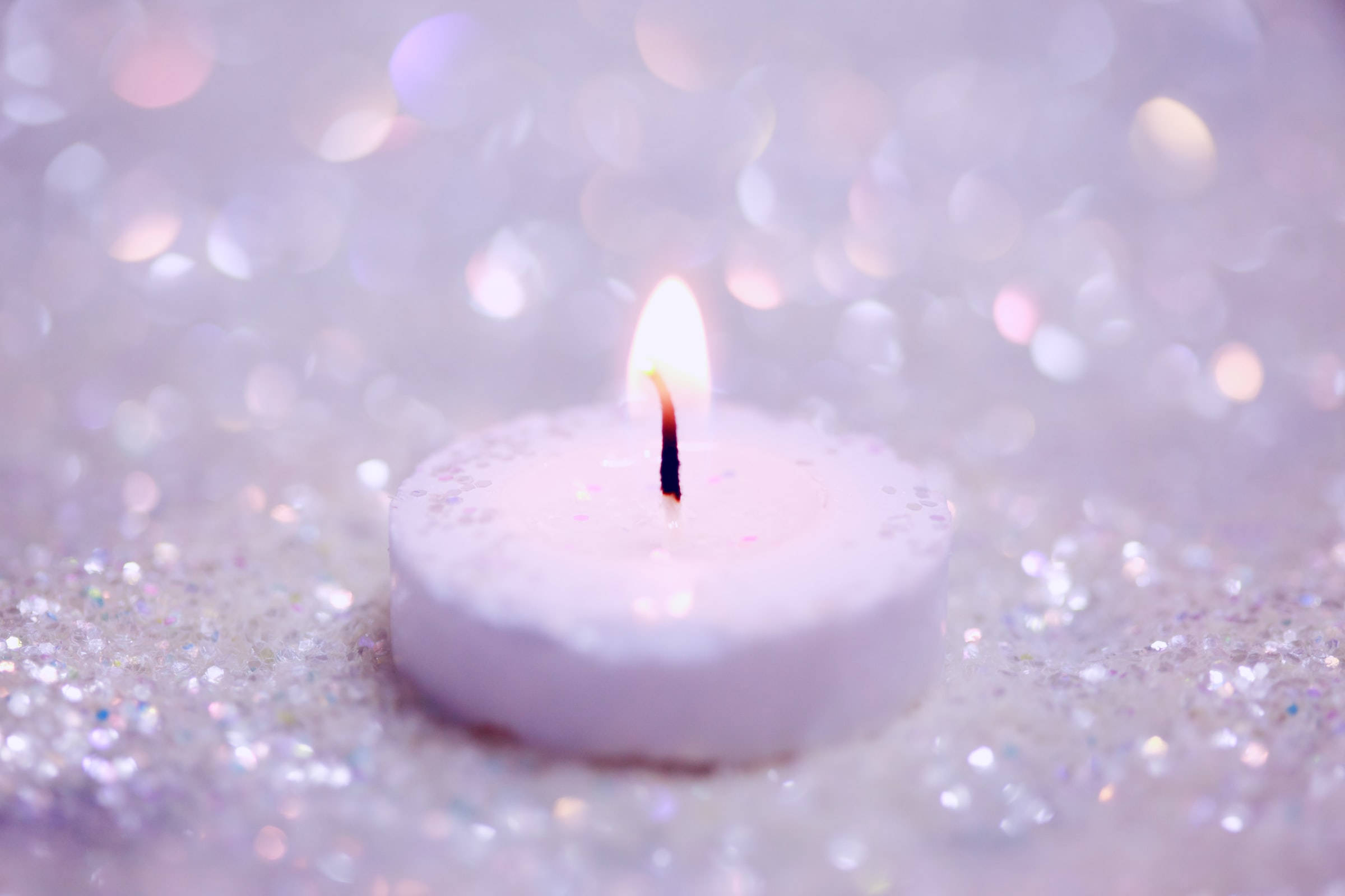 Remembrance 桌布 壁紙 — 一支點燃的白色蠟燭放在閃爍的銀色亮片上，背景有柔和散景光。