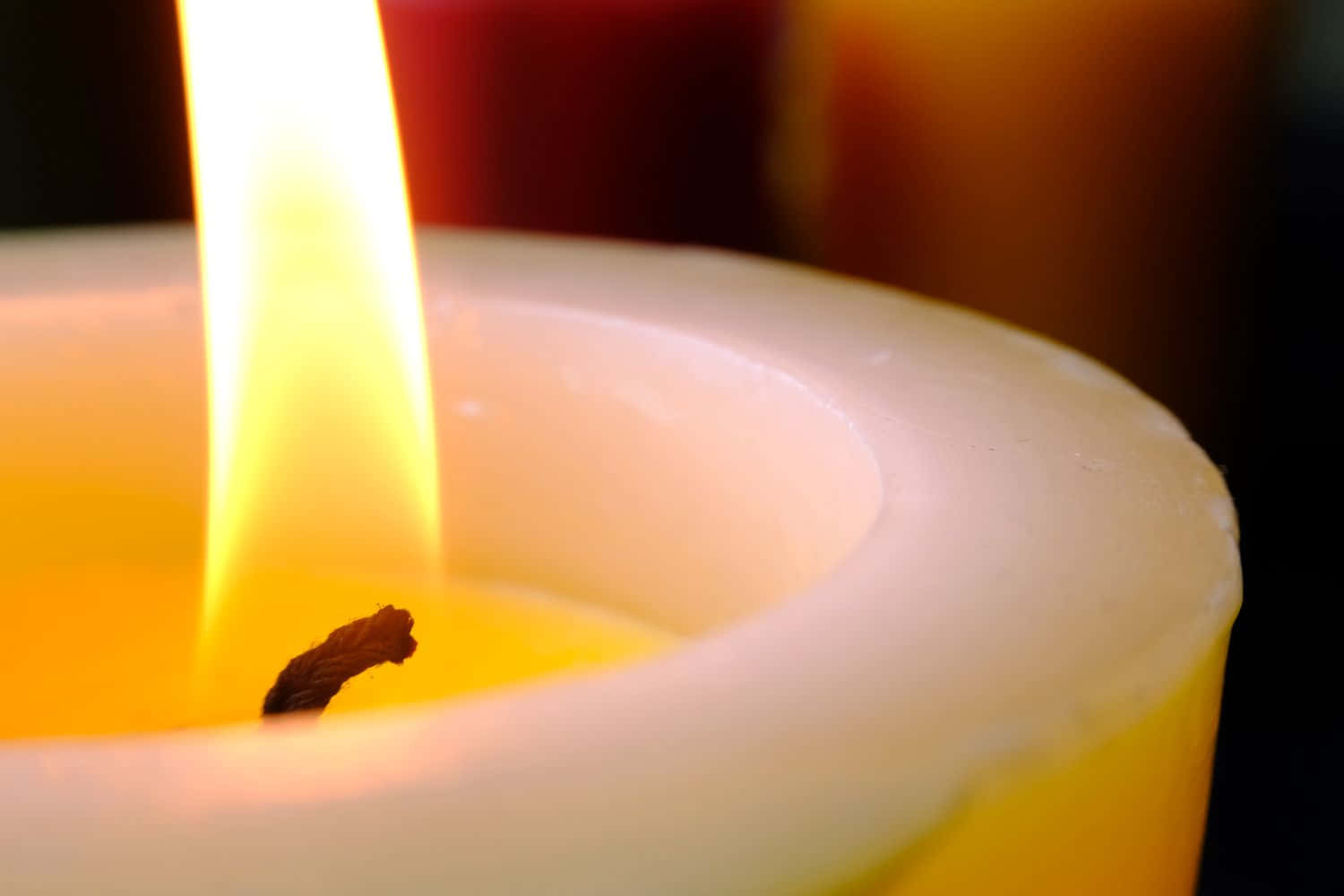 蠟燭 桌布 壁紙 — 一支點燃的白色蠟燭的特寫，明亮的黃色火焰在蠟燭表面投射出溫暖的光芒。