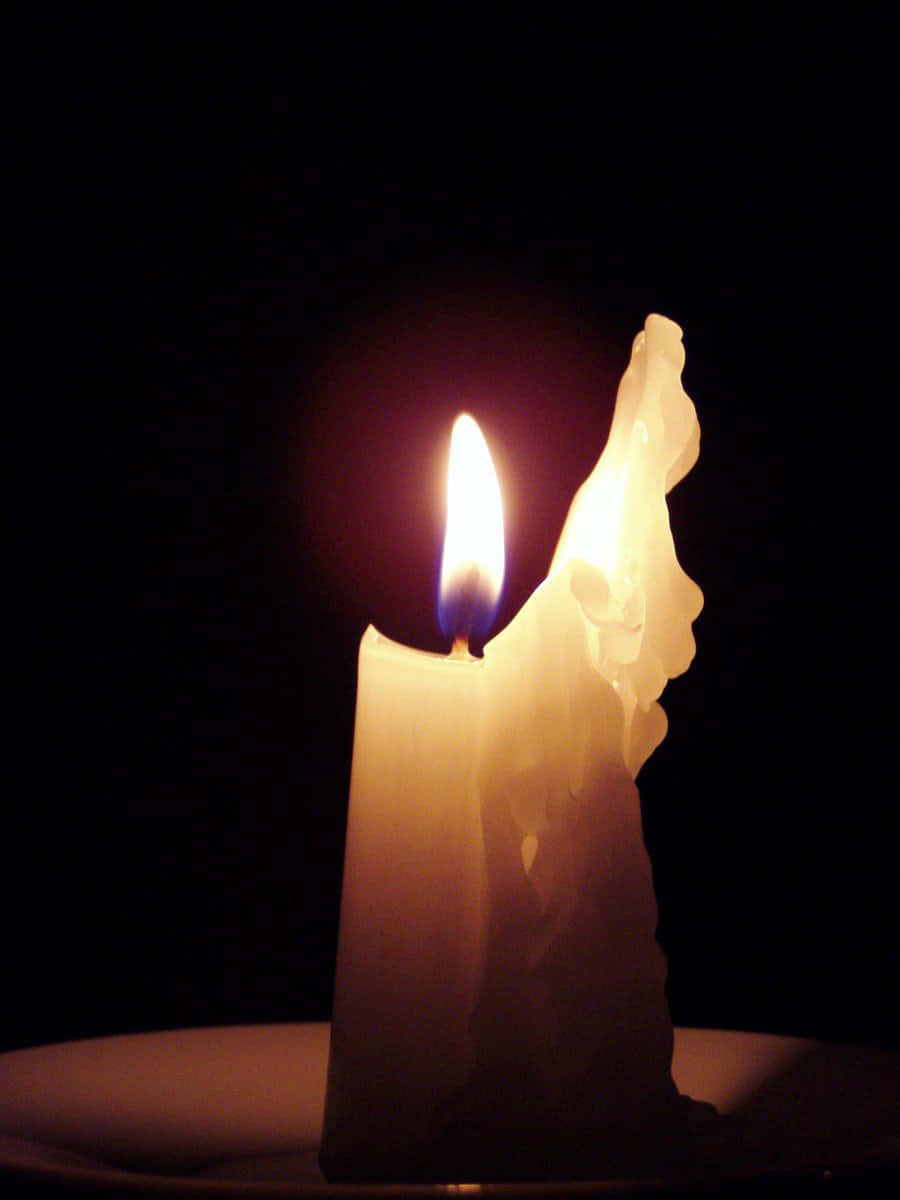 Candle Light 桌布 壁紙 — 一支點燃的蠟燭，帶有高聳的火焰和融化的蠟滴，映襯在純黑色背景上。