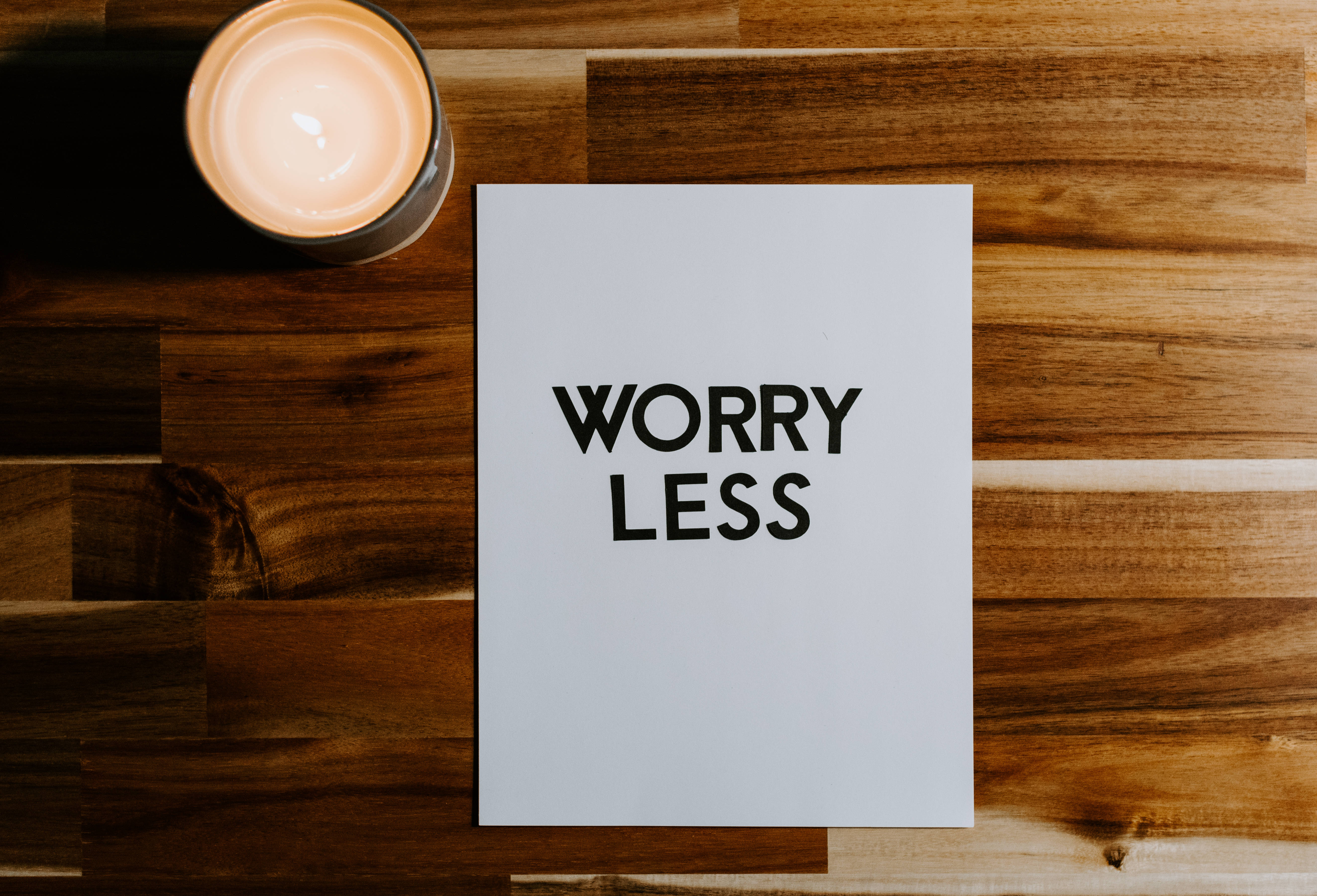 Motivation 桌布 壁紙 — 一支點燃的蠟燭在溫暖的木桌上，旁邊放著一張寫有「WORRY LESS」的白色卡片，閃爍著光芒。