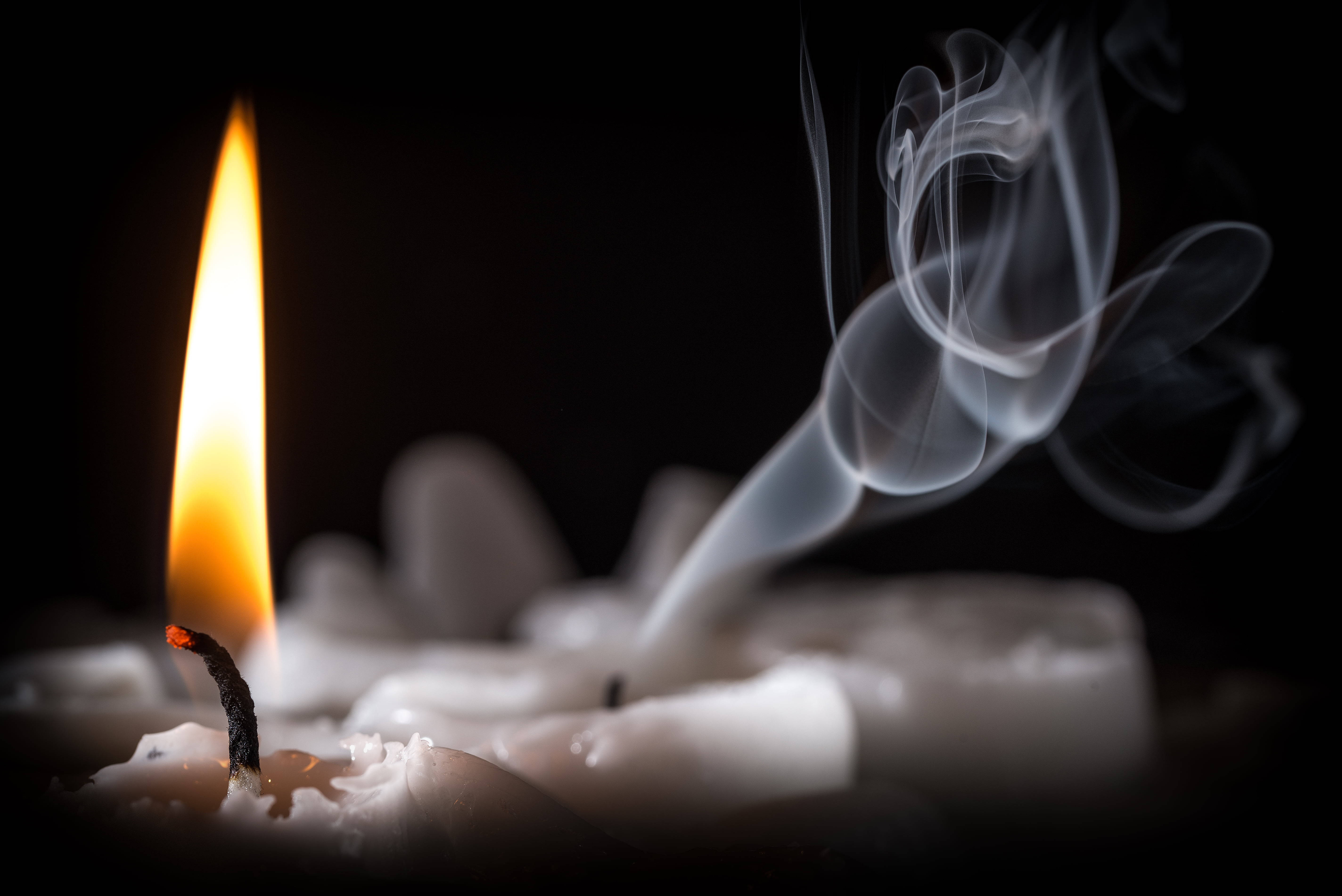 火焰動畫 桌布 壁紙 — 一支點燃的蠟燭在黑色背景上散發出溫暖的光芒，蠟燭的蠟上昇起旋轉的煙霧。