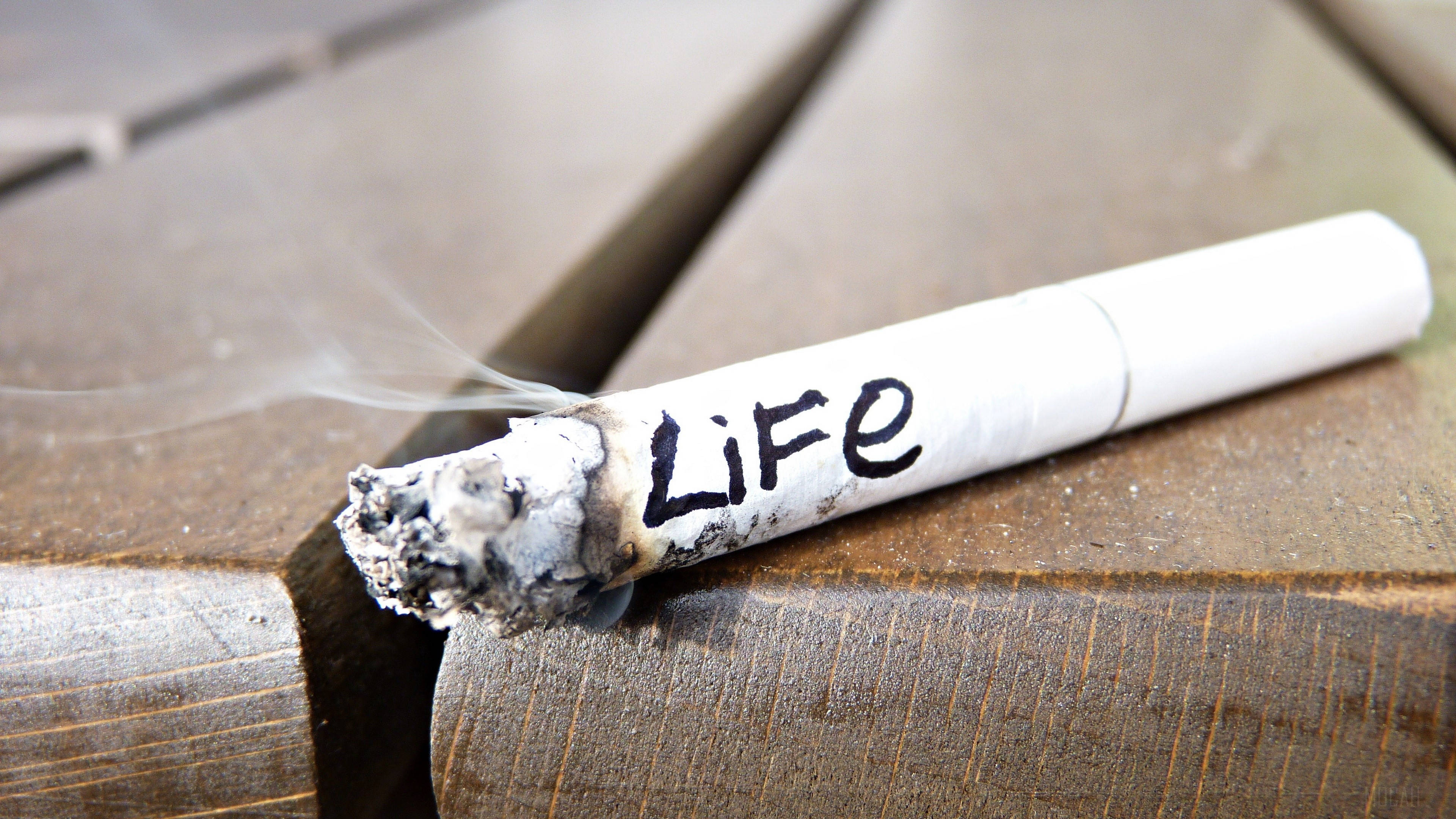 life 桌布 壁紙 — 一支點燃的香煙上寫著「Life」，在風化的木質表面上冒煙。