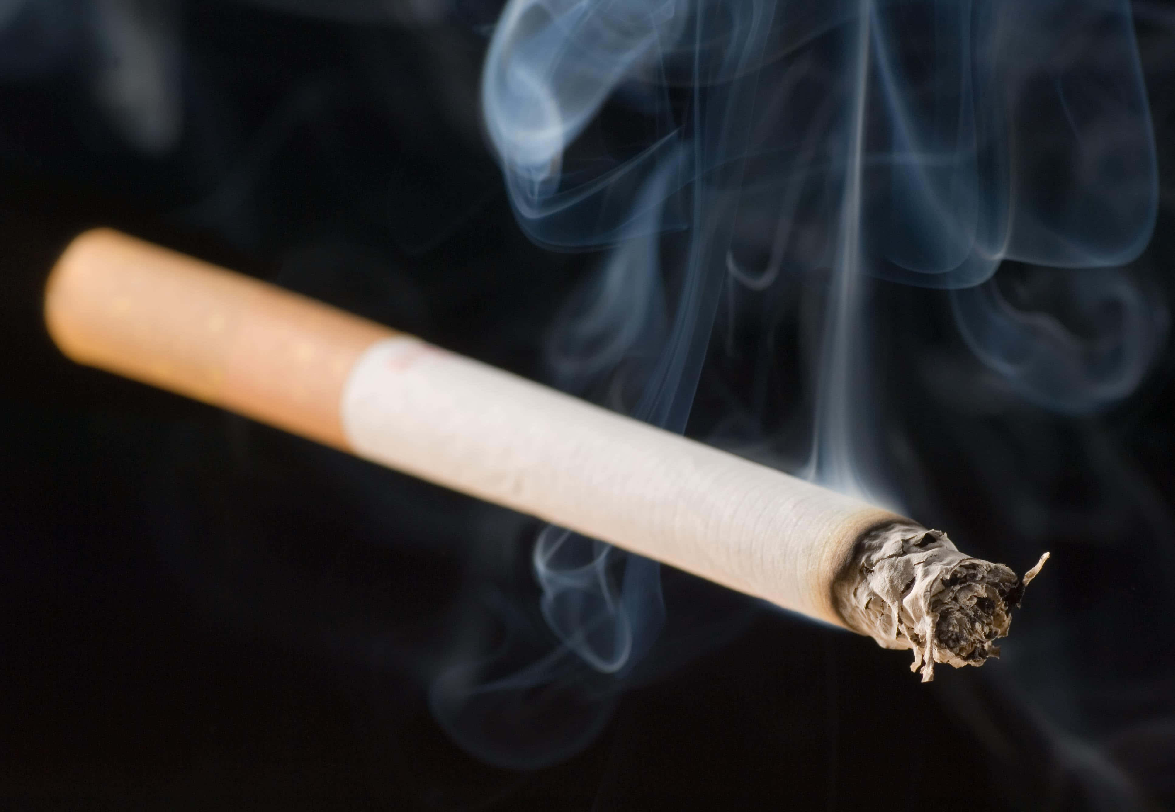 cigarettes 桌布 壁紙 — 一支點燃的香煙在黑色背景上悶燒，縷縷煙霧向上盤旋。